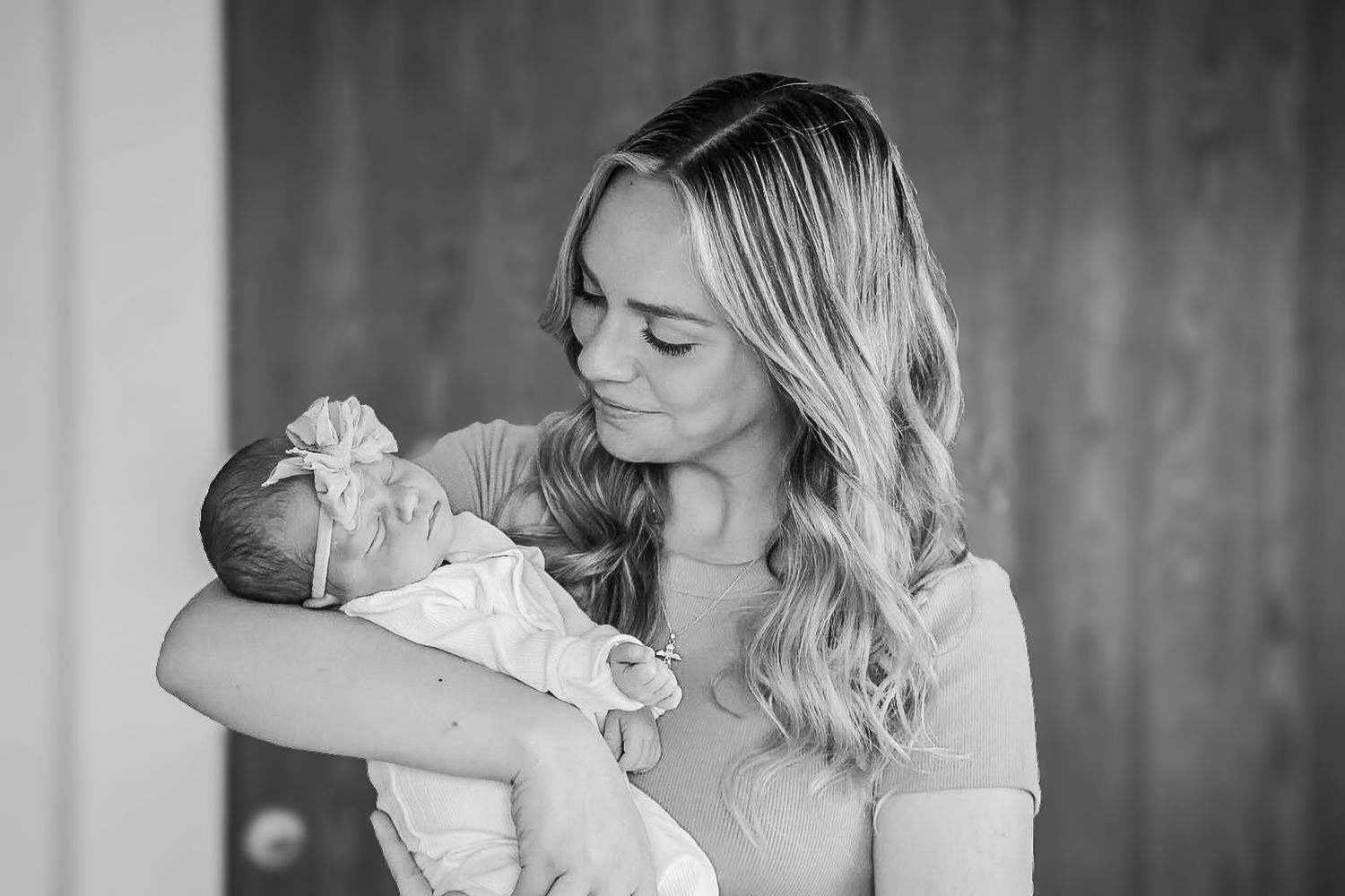 Black and white portrait of blonde mother tenderly cradling her newborn baby in her arms indoors.