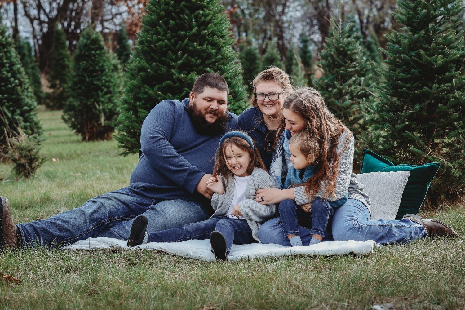 Happy family of five sits together on a blanket at a Christmas tree farm.