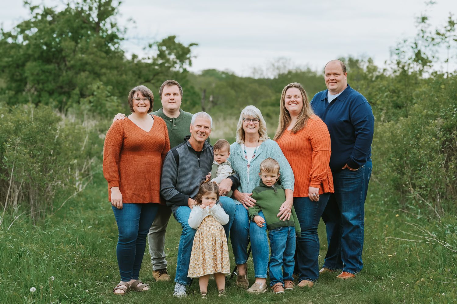 A large multigenerational family poses together smiling in a lush green outdoor field.