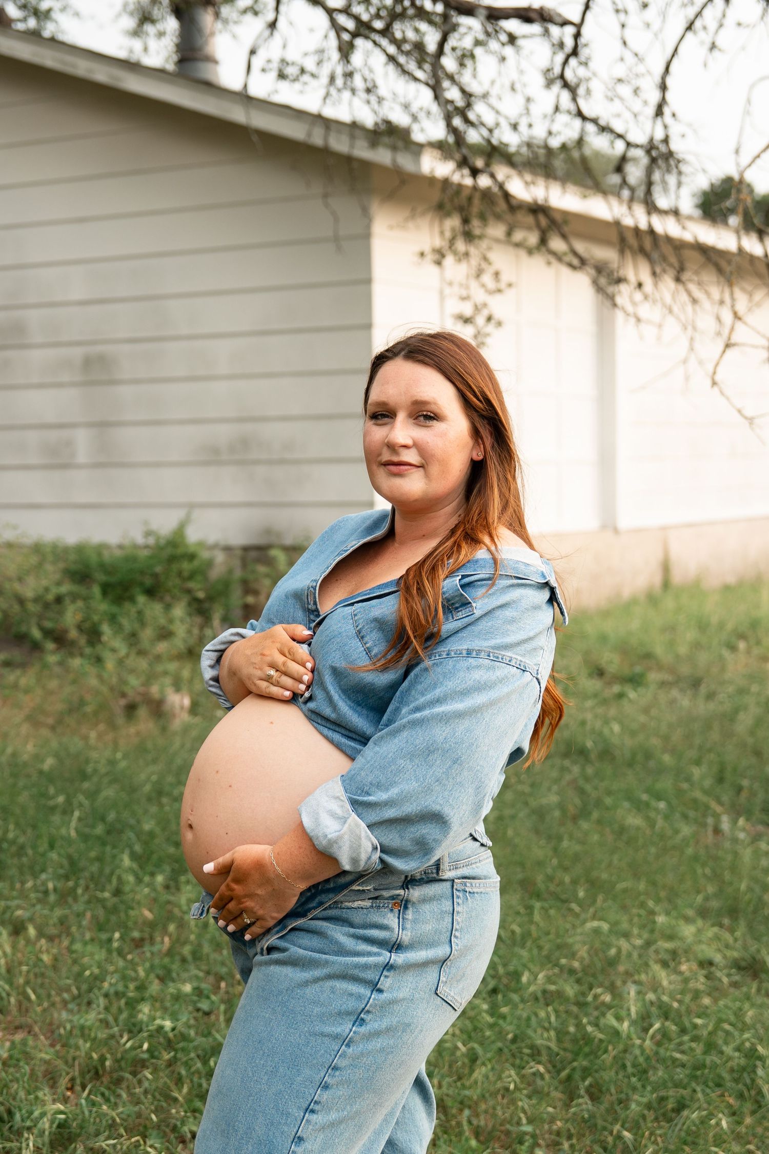 A pregnant woman in denim sits on grass while cradling her baby bump in a series of candid outdoor maternity photos.