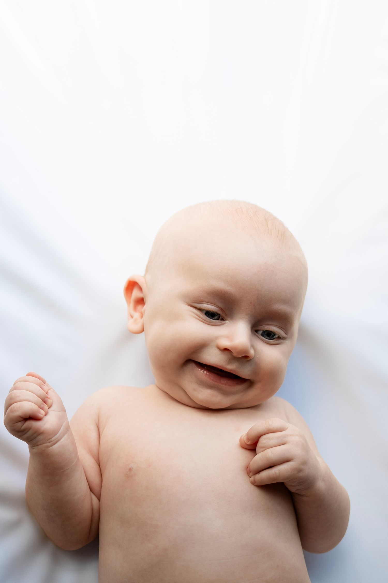 A happy baby lying on white bedding shows different facial expressions in a series of four connected photos.