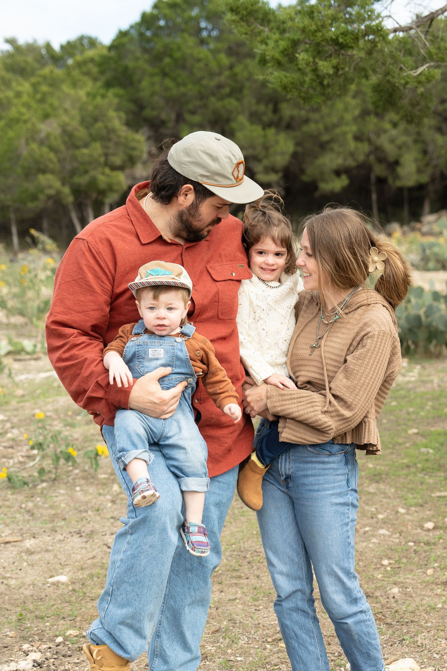 Family in casual denim and warm sweaters share tender moments together outdoors against a natural backdrop.