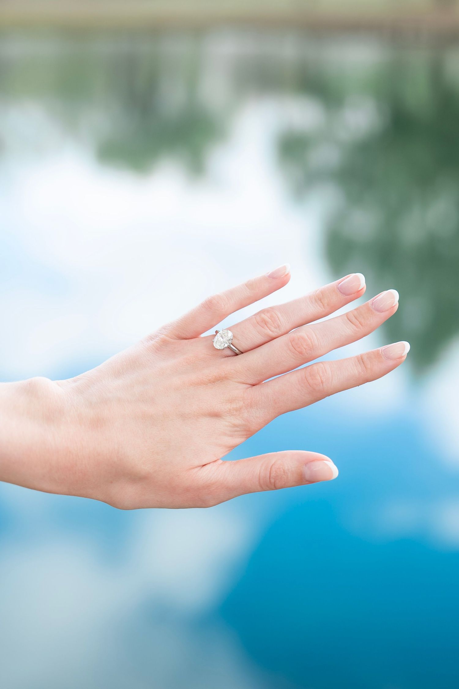 A delicate hand with a silver ring extends gracefully against a soft blue and white blurred background.