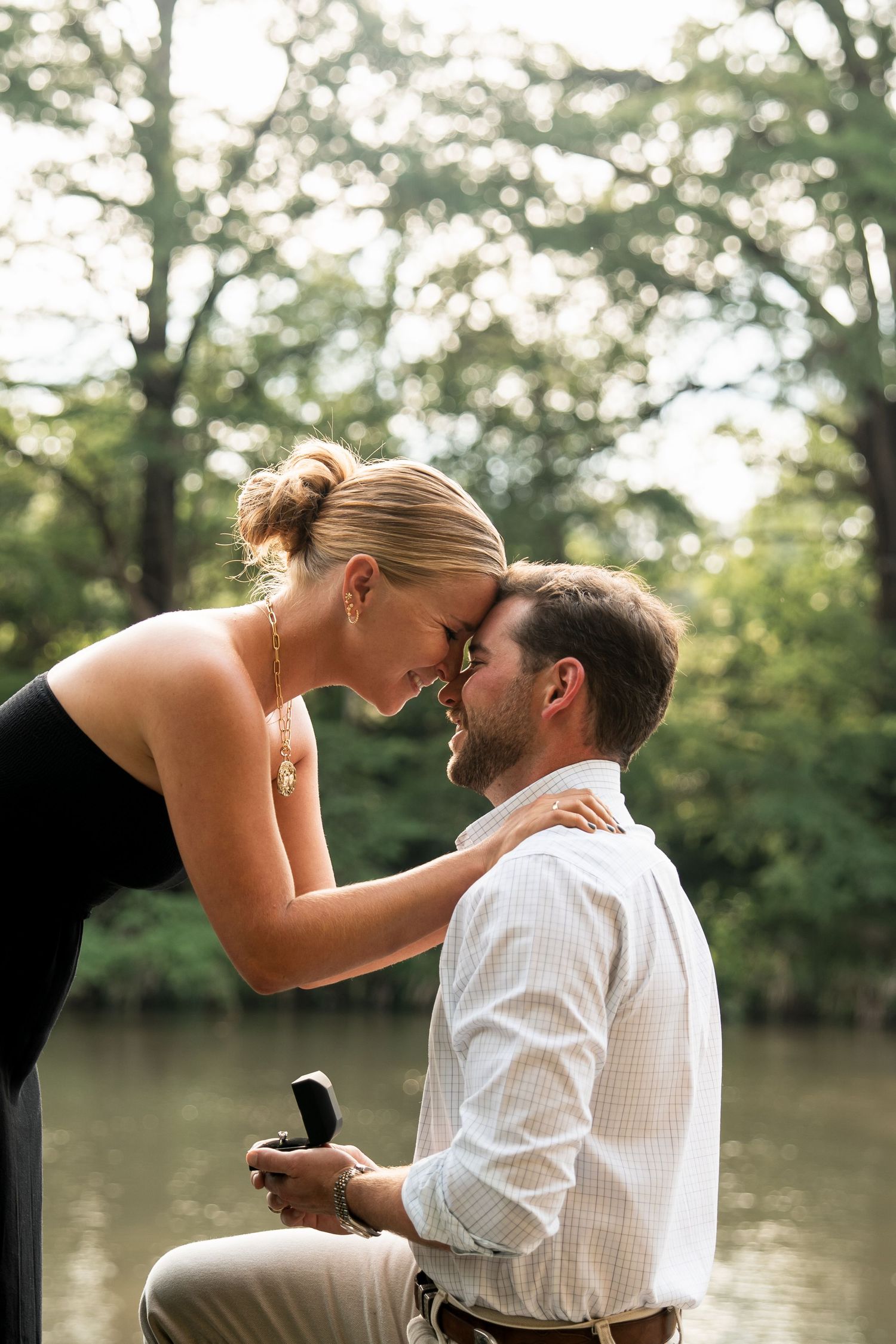 A romantic couple shares tender moments by a serene lake during an engagement photoshoot in natural lighting.