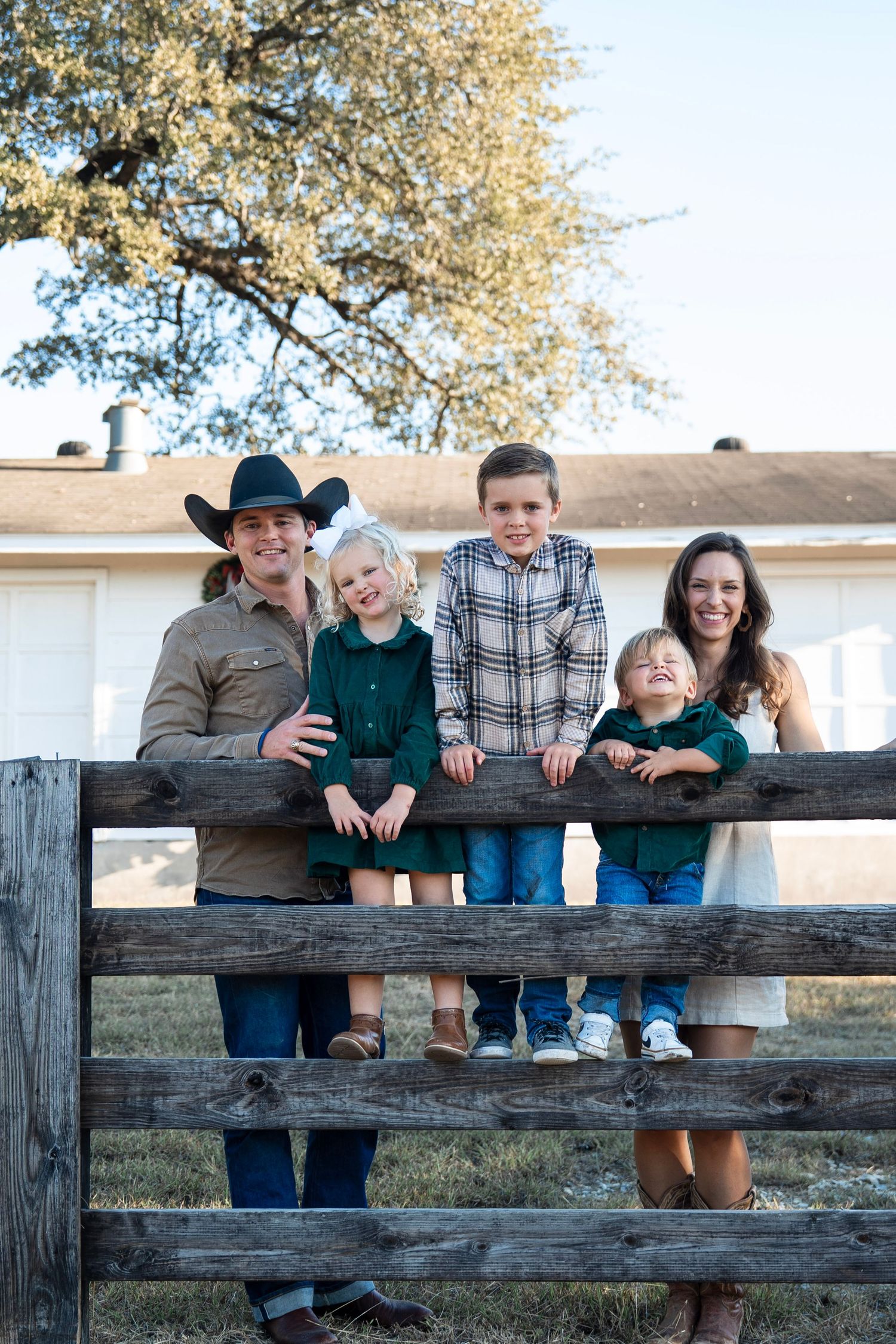 A group sits together on a rustic wooden fence in an outdoor setting during golden hour.