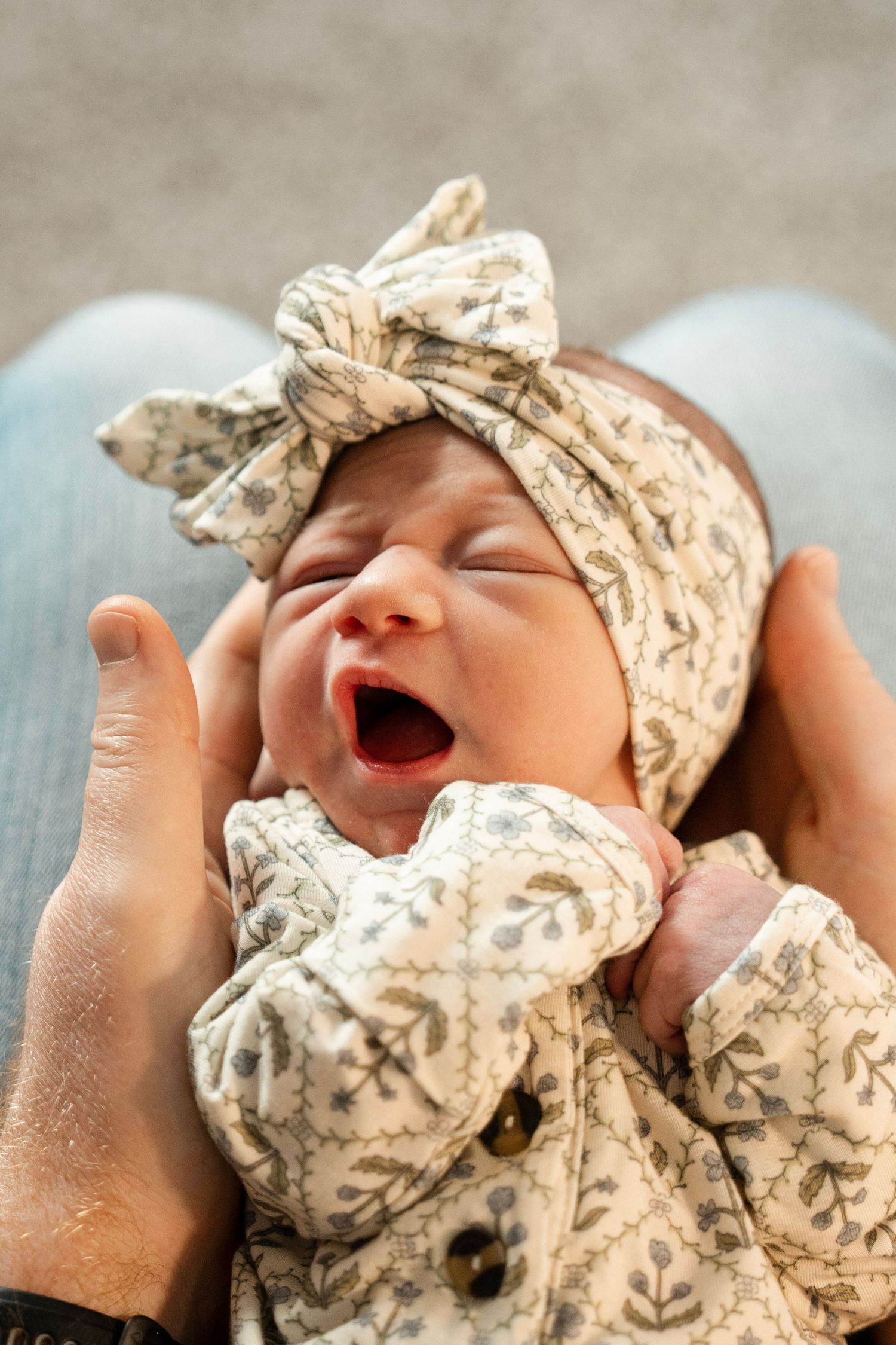 A sleeping newborn baby swaddled in a floral print blanket and matching hat rests peacefully.