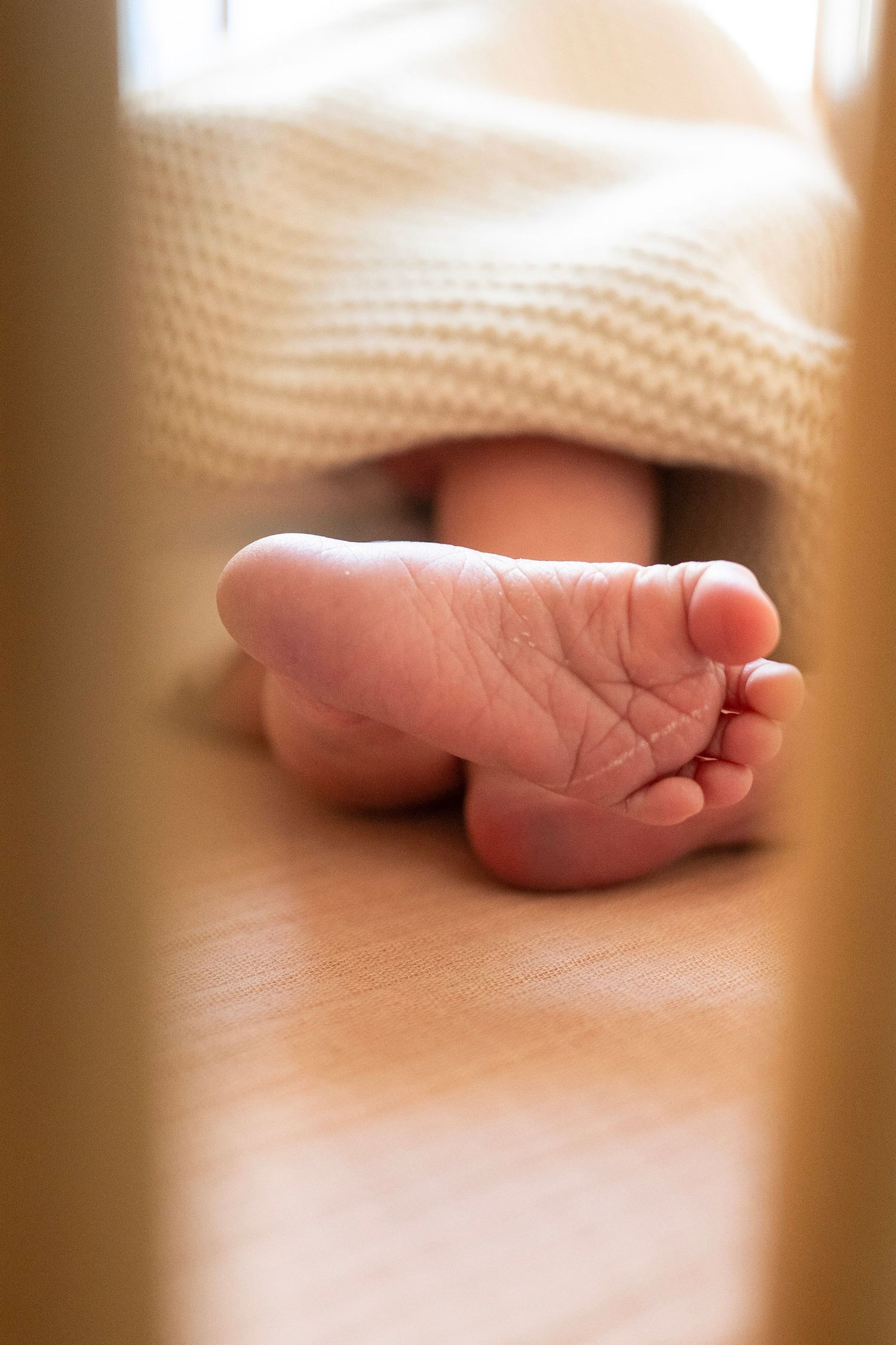 Close-up view of a tiny newborn baby foot resting on a soft beige blanket in natural lighting.