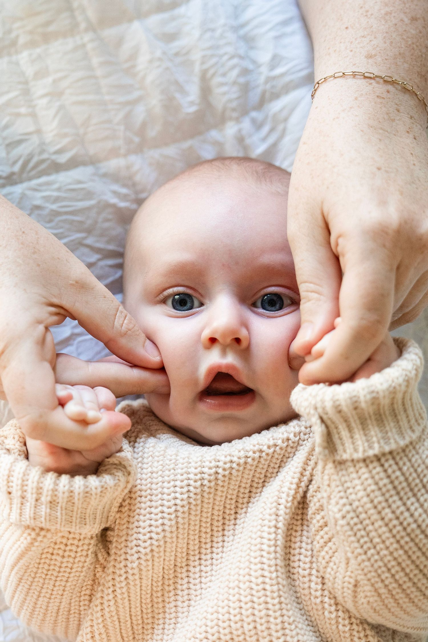 A series of four close-up photos showing playful peekaboo moments with a baby in a cream knit sweater.