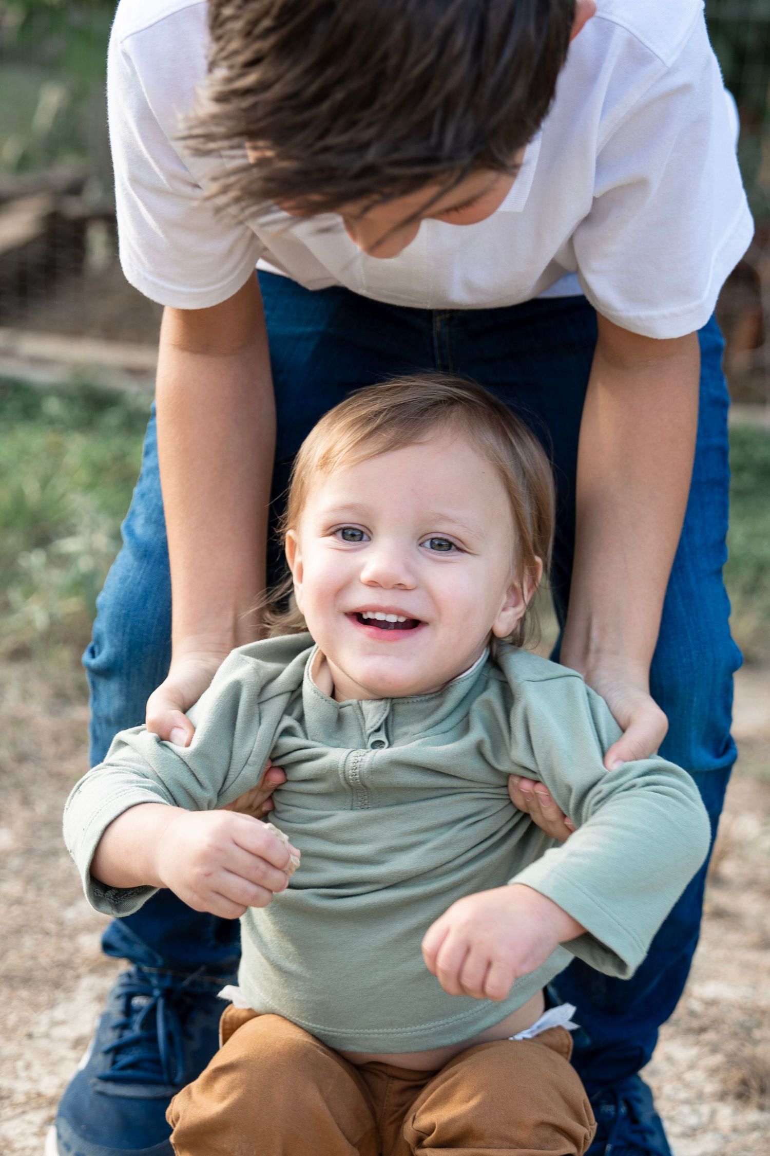 A series of progressive photos showing a small child in a sage green shirt and brown pants being tickled while sitting outdoors.