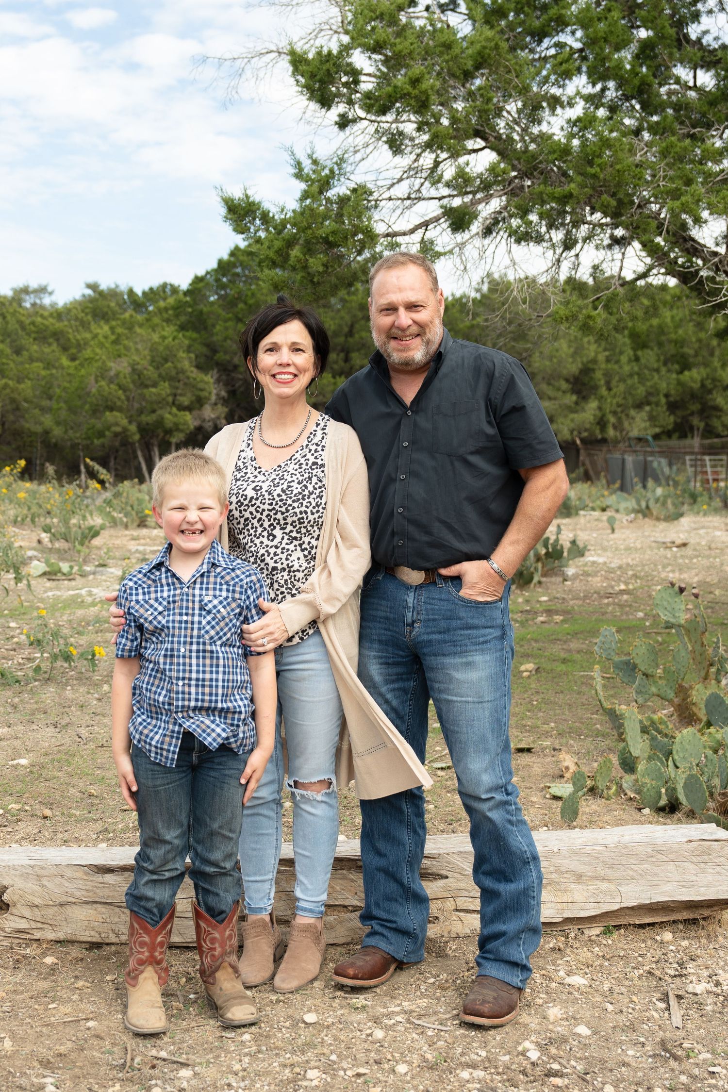 A family poses together on a rustic wooden platform surrounded by desert brush and cacti in an outdoor setting.