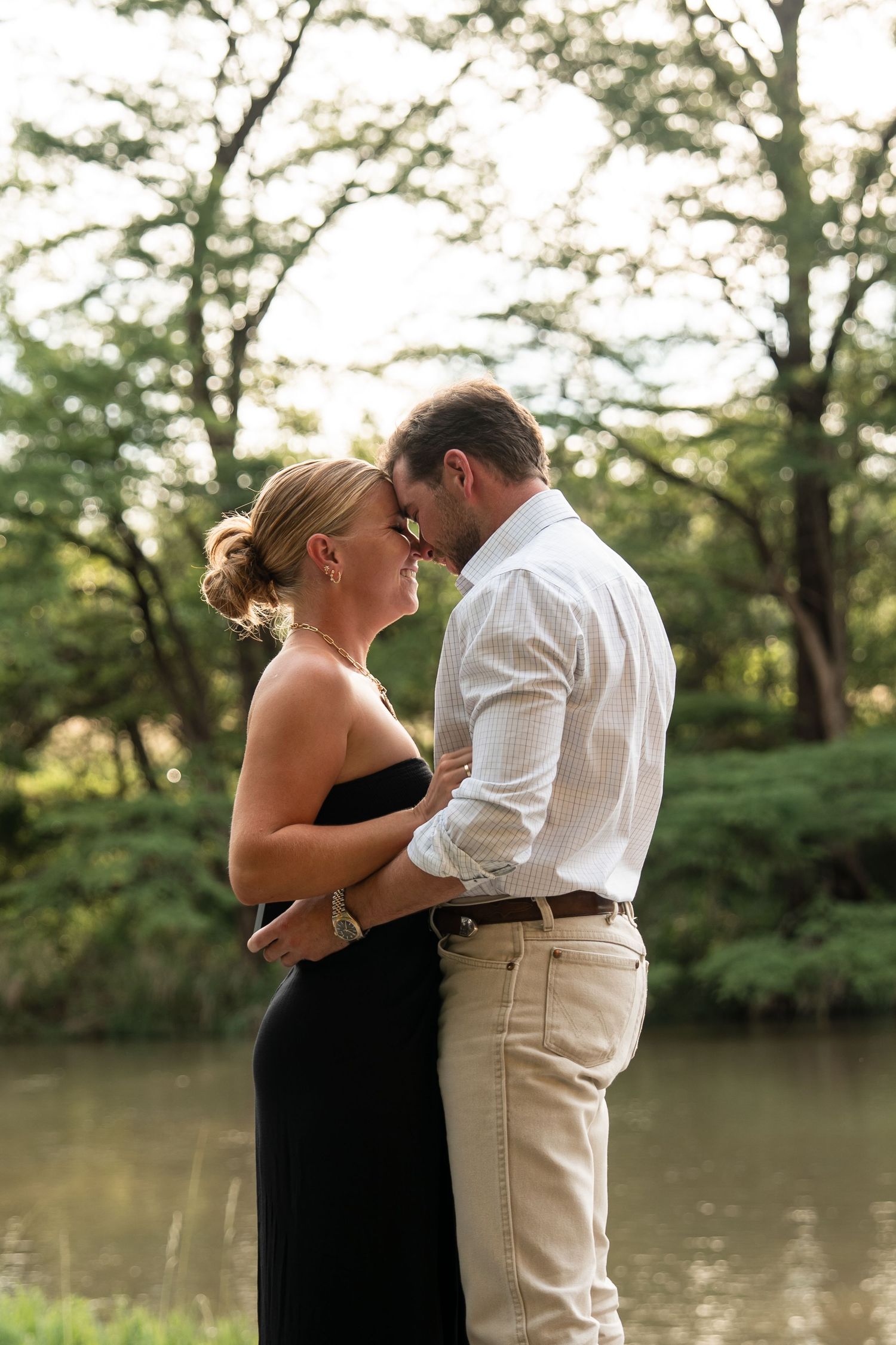 A romantic couple shares an intimate moment by a tranquil lake during a sunset photo session.