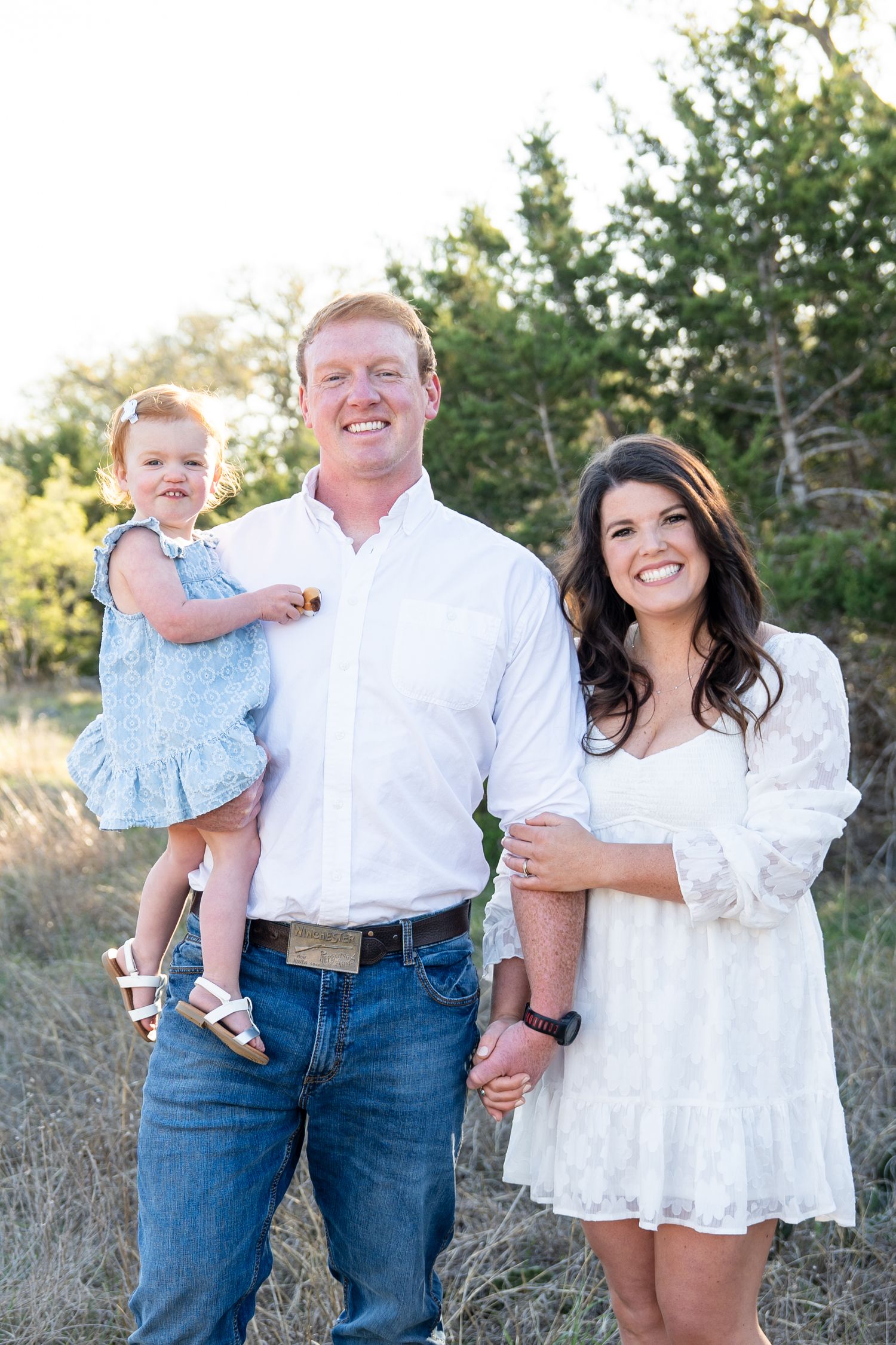 Family wearing white outfits poses together outdoors in a natural setting during golden hour.
