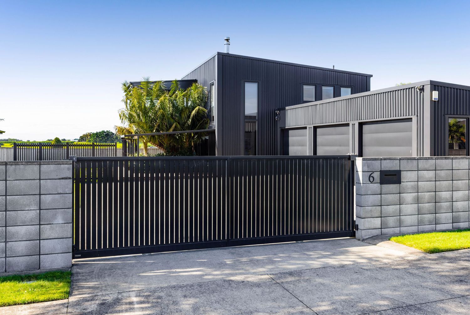 Modern black house exterior with sleek sliding gate and concrete block fence in contemporary residential setting.