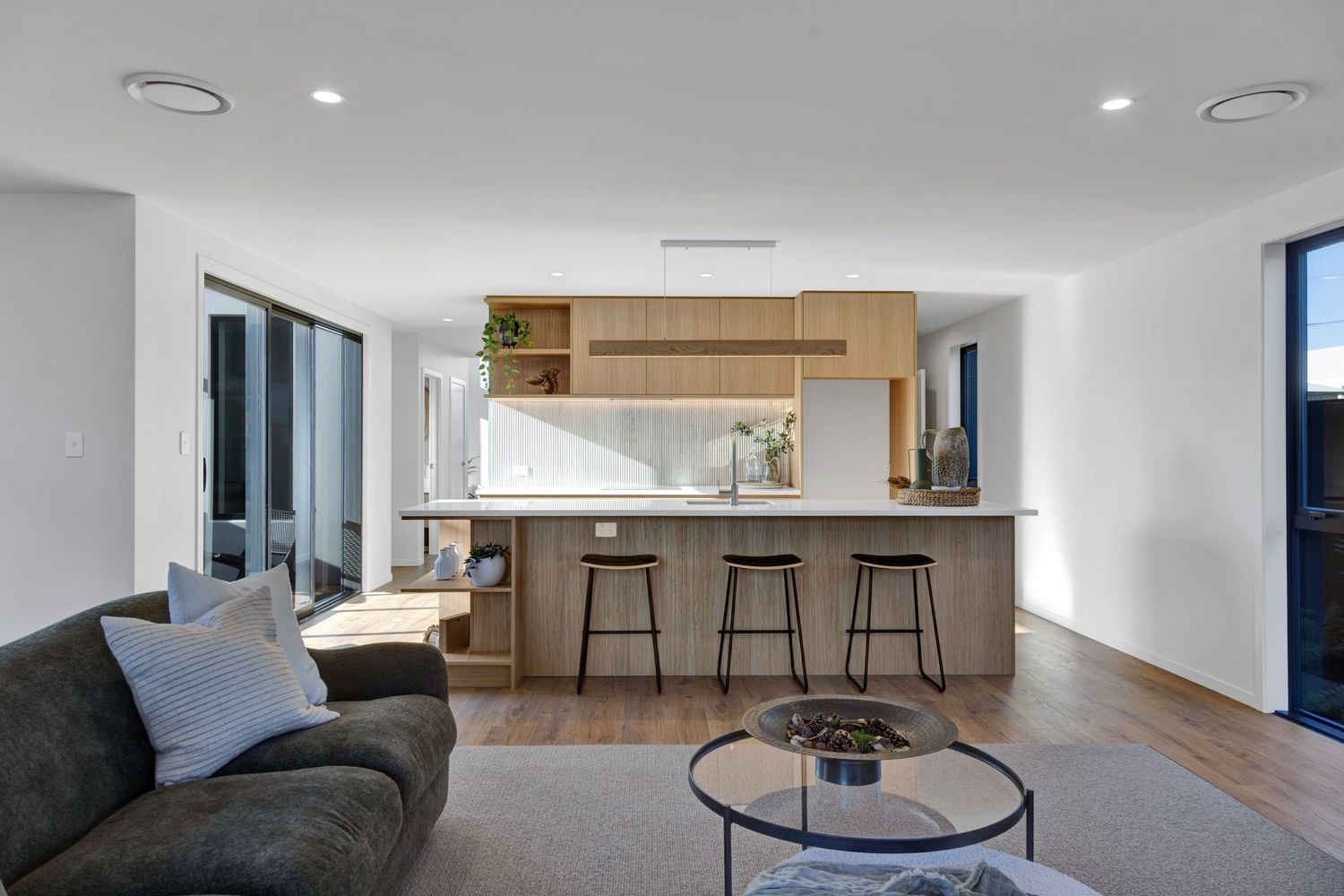 A sleek, modern open-concept living space with white walls, minimalist furniture, and wood flooring illuminated by recessed lighting.