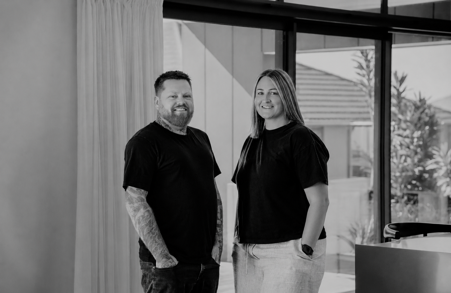 Two professionals in black attire pose together in a modern, well-lit interior space.