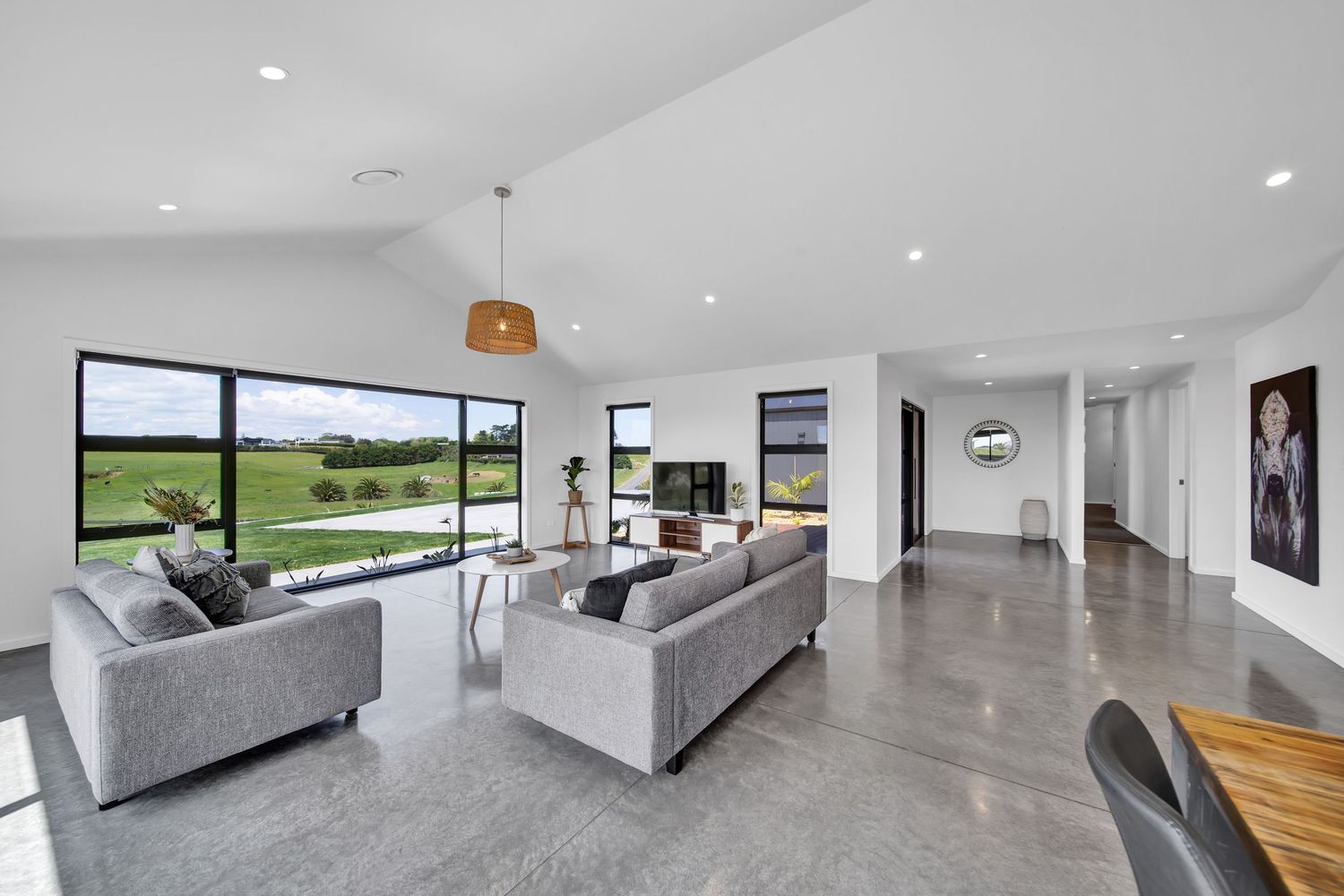 Modern minimalist living room with polished concrete floors and floor-to-ceiling windows overlooking green landscape.