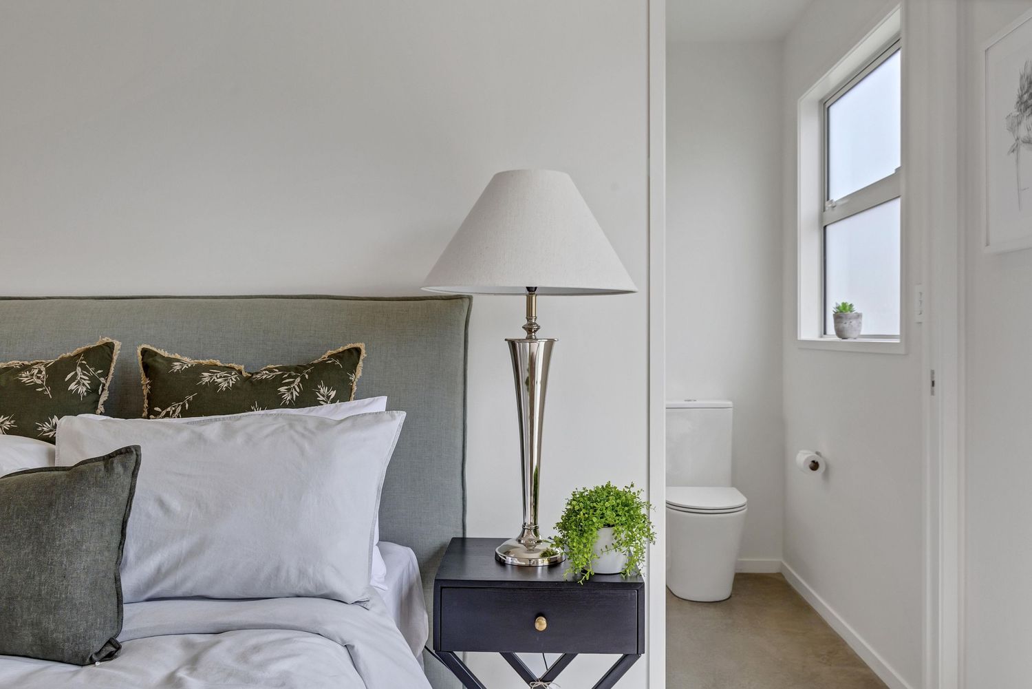 A bright, minimalist bedroom features white walls, modern furnishings, and natural light streaming through windows.