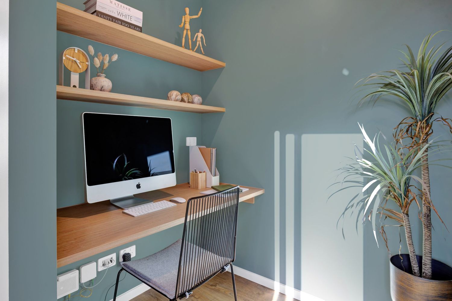 Minimalist home office setup with wooden shelves and desk against blue-gray wall.