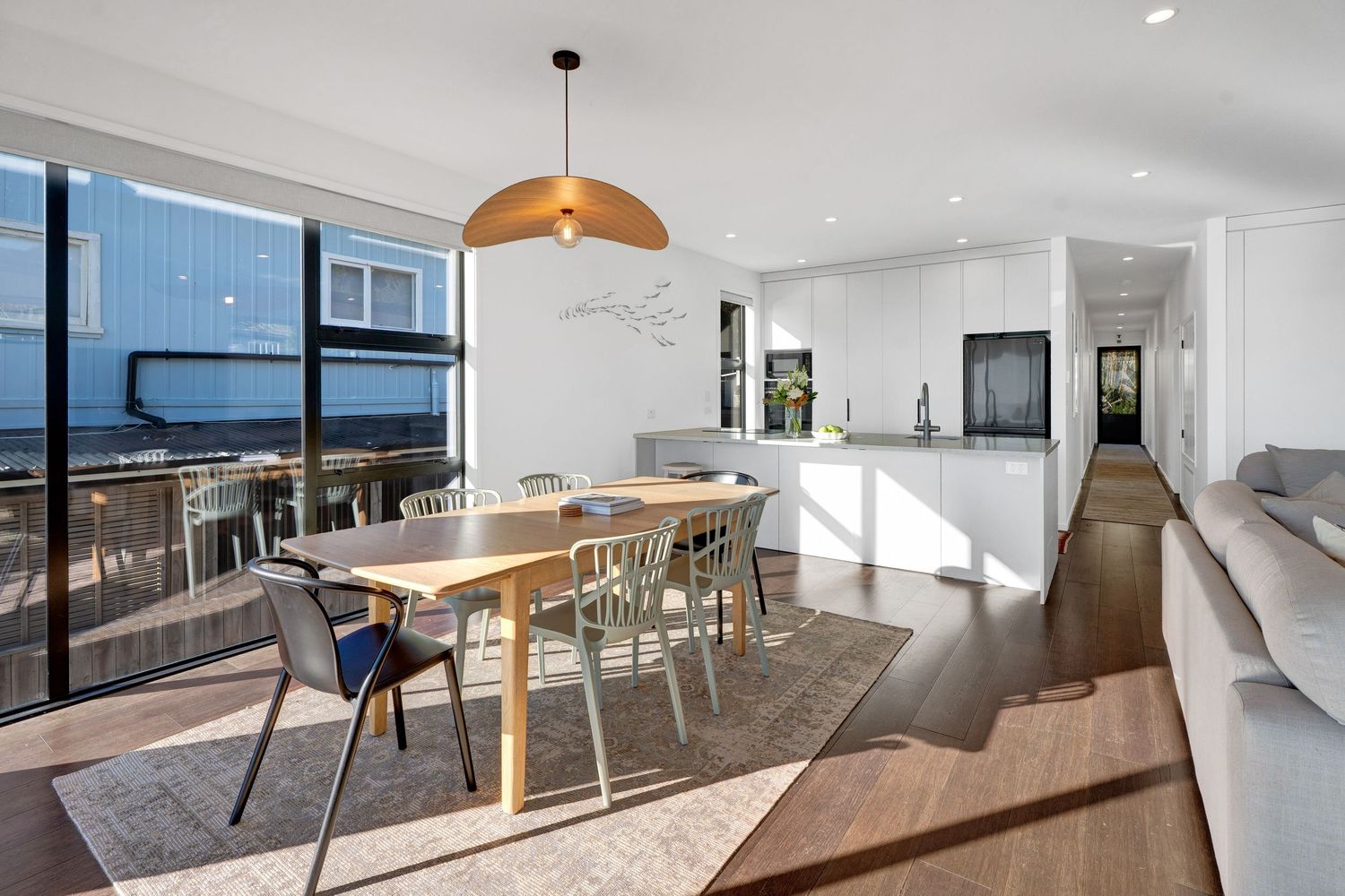 Modern apartment interior with hardwood floors, white walls, and large windows showcasing natural light and city views.