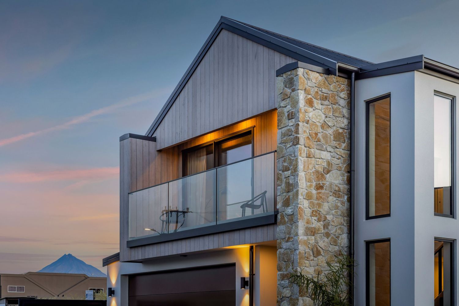Modern architectural home with stone feature wall and glass balcony at sunset.