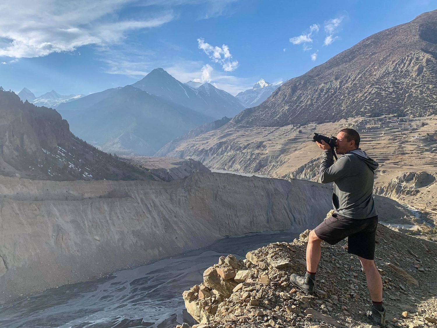 Photographer standing on a rocky ledge photographing a glacier and distant mountains. Nepal, Himalayas