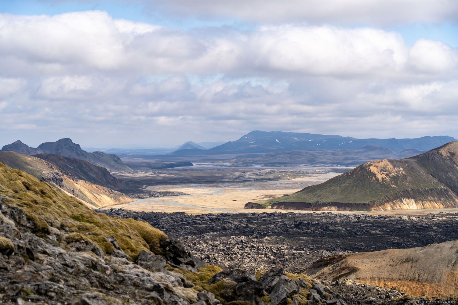 Expansive volcanic highland valley with rugged lava fields and distant mountain ranges under a cloudy sky. Iceland