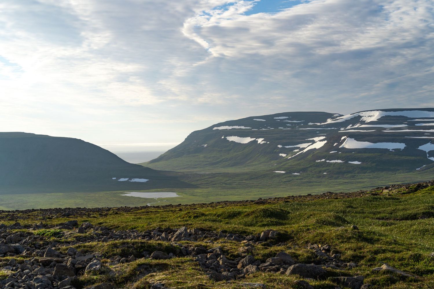Broad highland valley with snow-streaked hills and open tundra in the foreground. Iceland