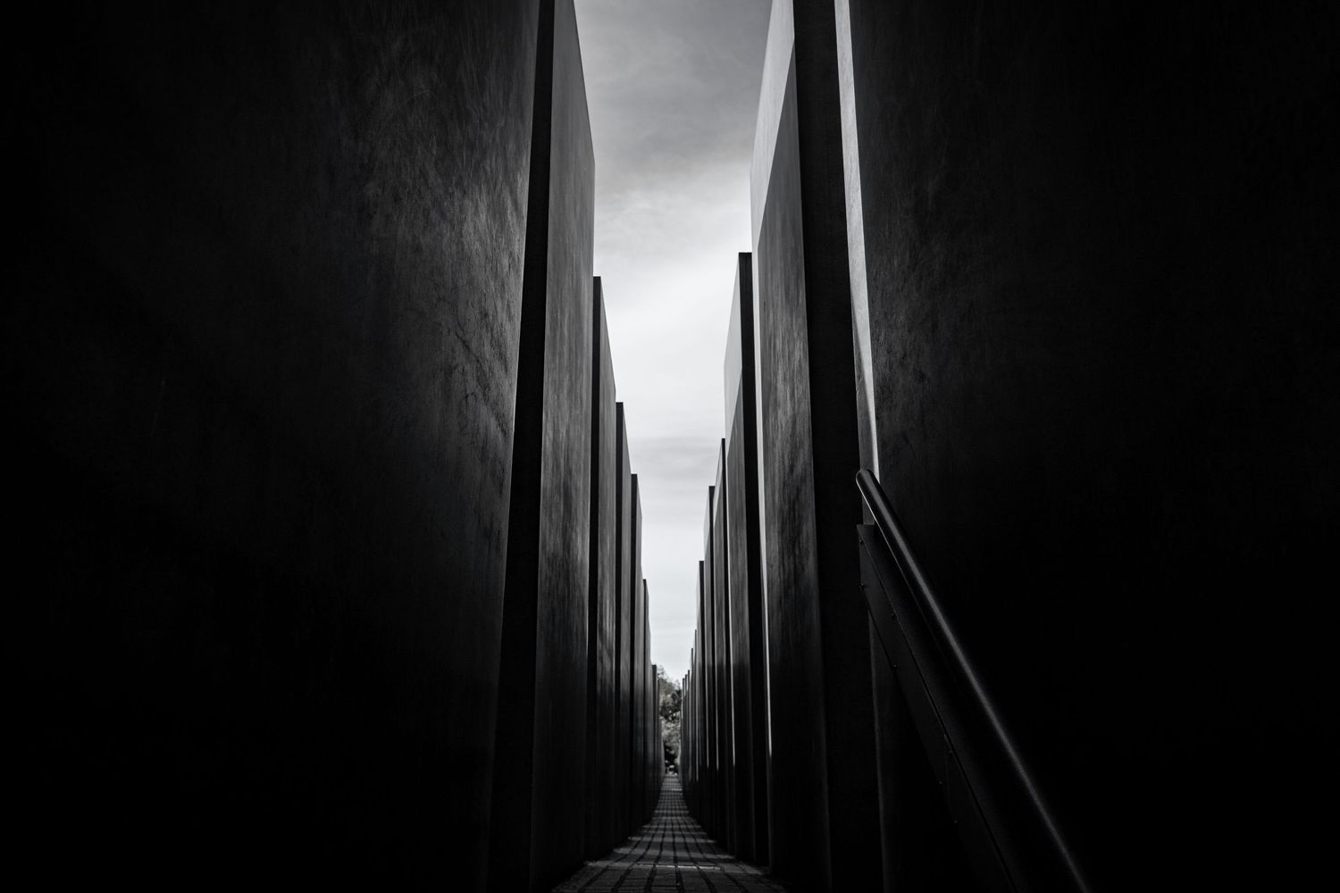 Black and white view down a narrow corridor between tall concrete memorial blocks