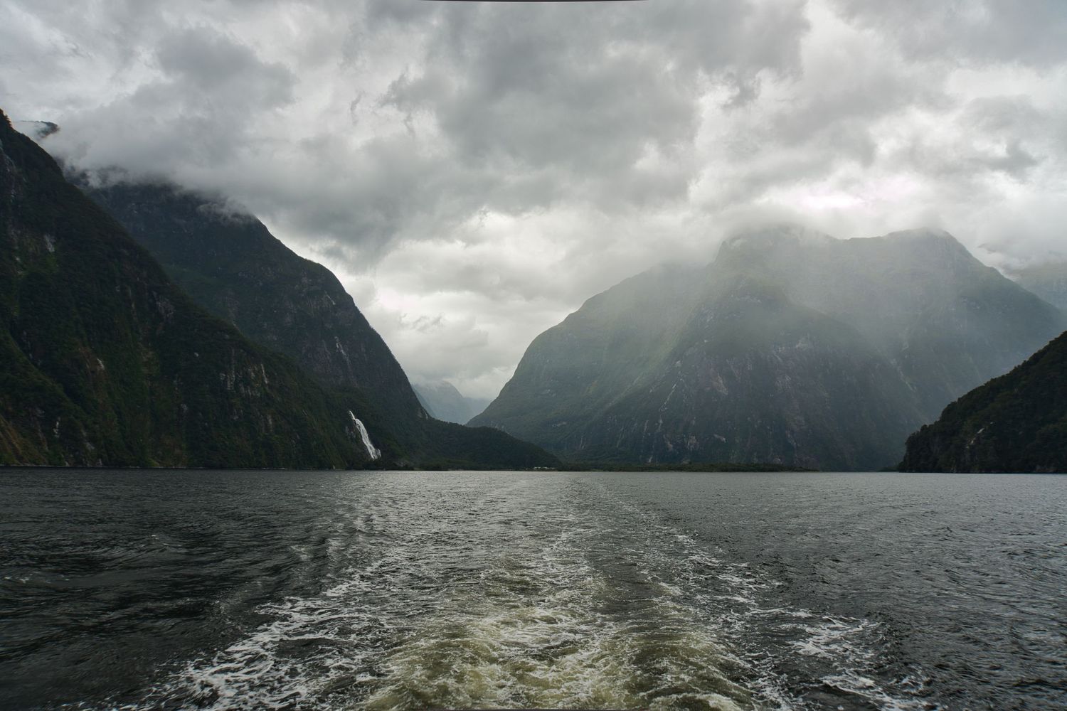 Moody fjord with steep mountains rising from calm water under heavy grey clouds at Milford Sound, New Zealand