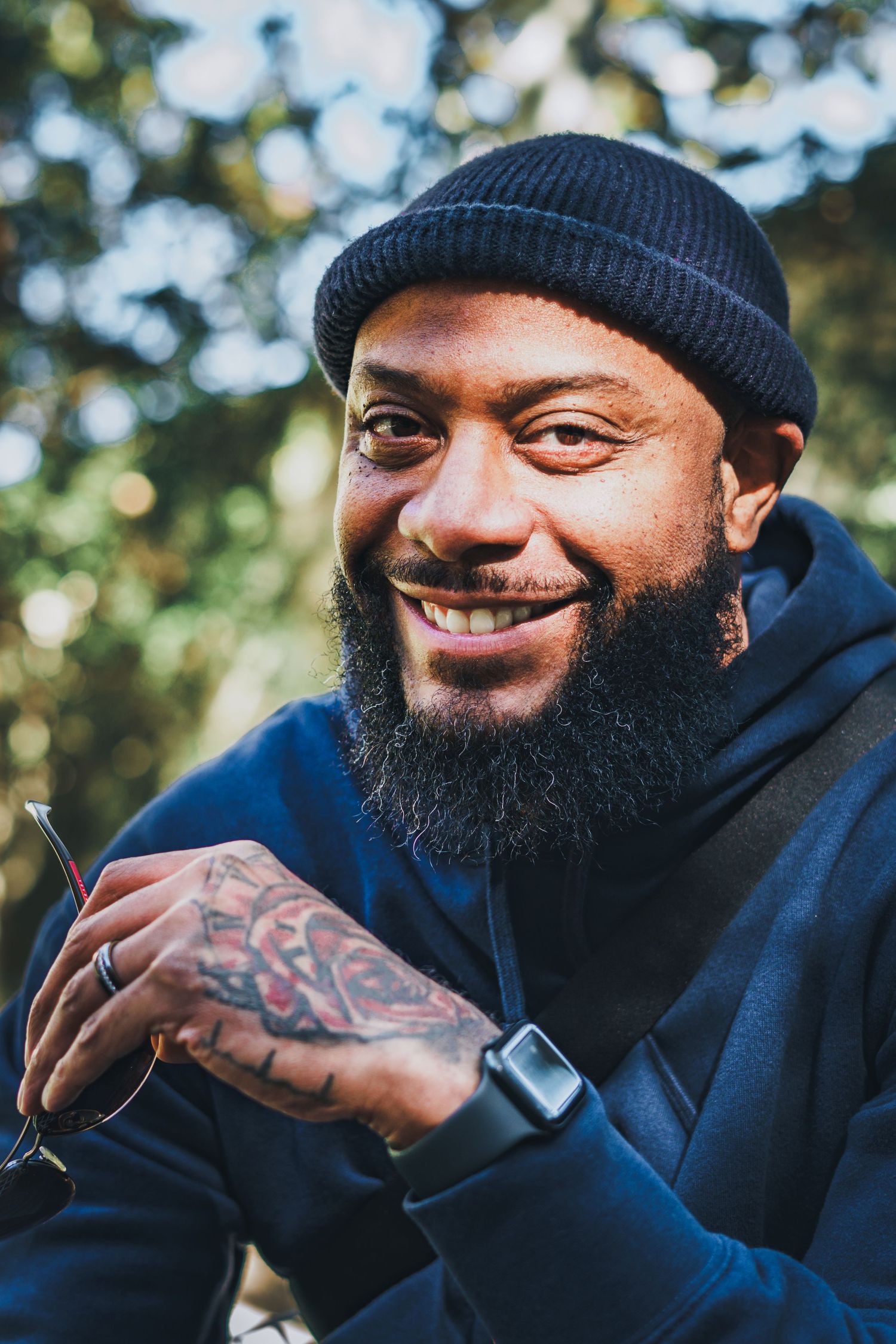 Portrait of someone in dark clothing and beanie against blurred nature background.