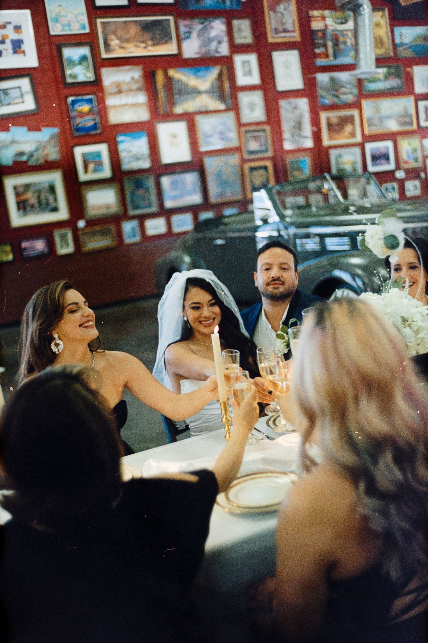Wedding party toasting and celebrating at a table with picture-covered walls.