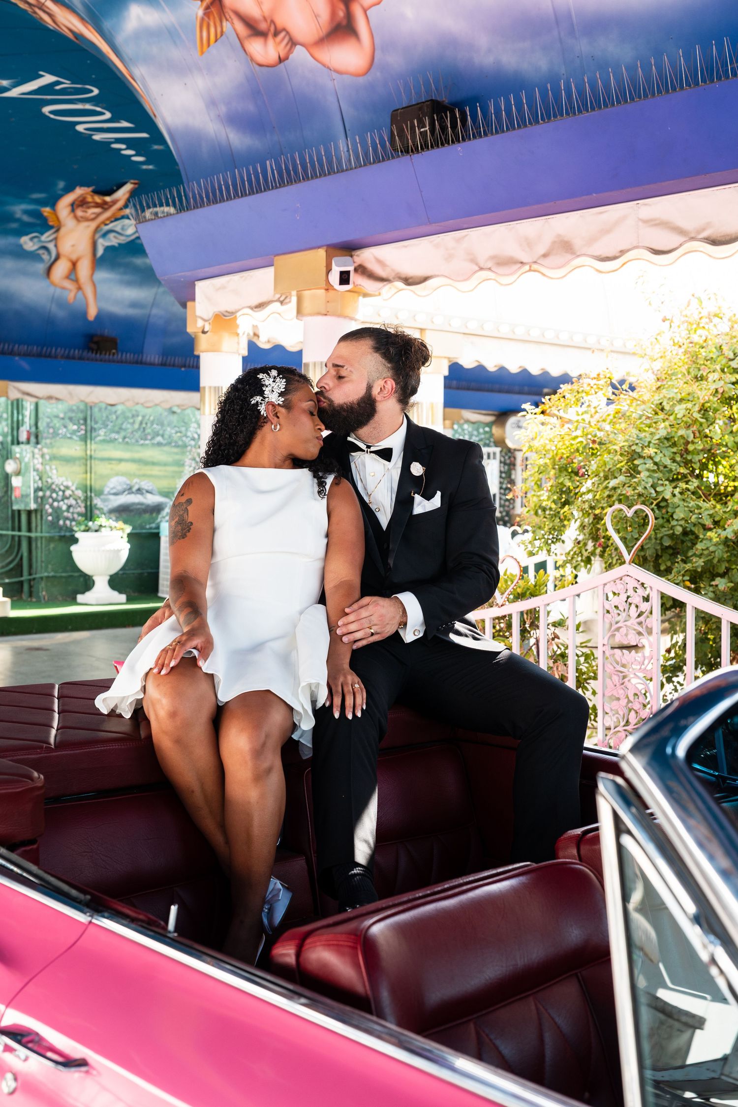 Newlyweds share intimate moments in the backseat of a pink classic car.