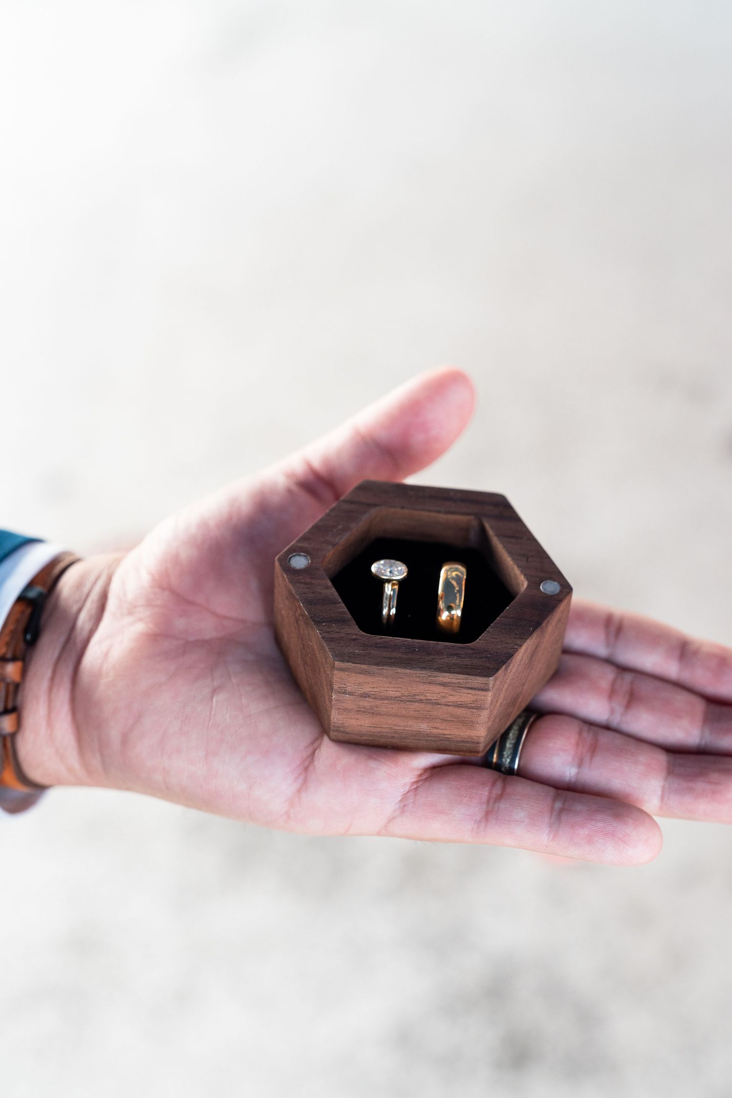 Small wooden hexagonal ring box held in an outstretched palm.