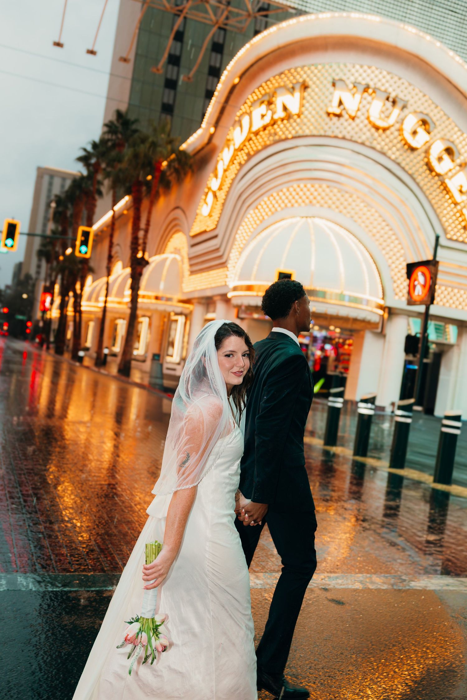 Bride and groom holding hands outside the Golden Nugget casino in Las Vegas on a rainy evening.