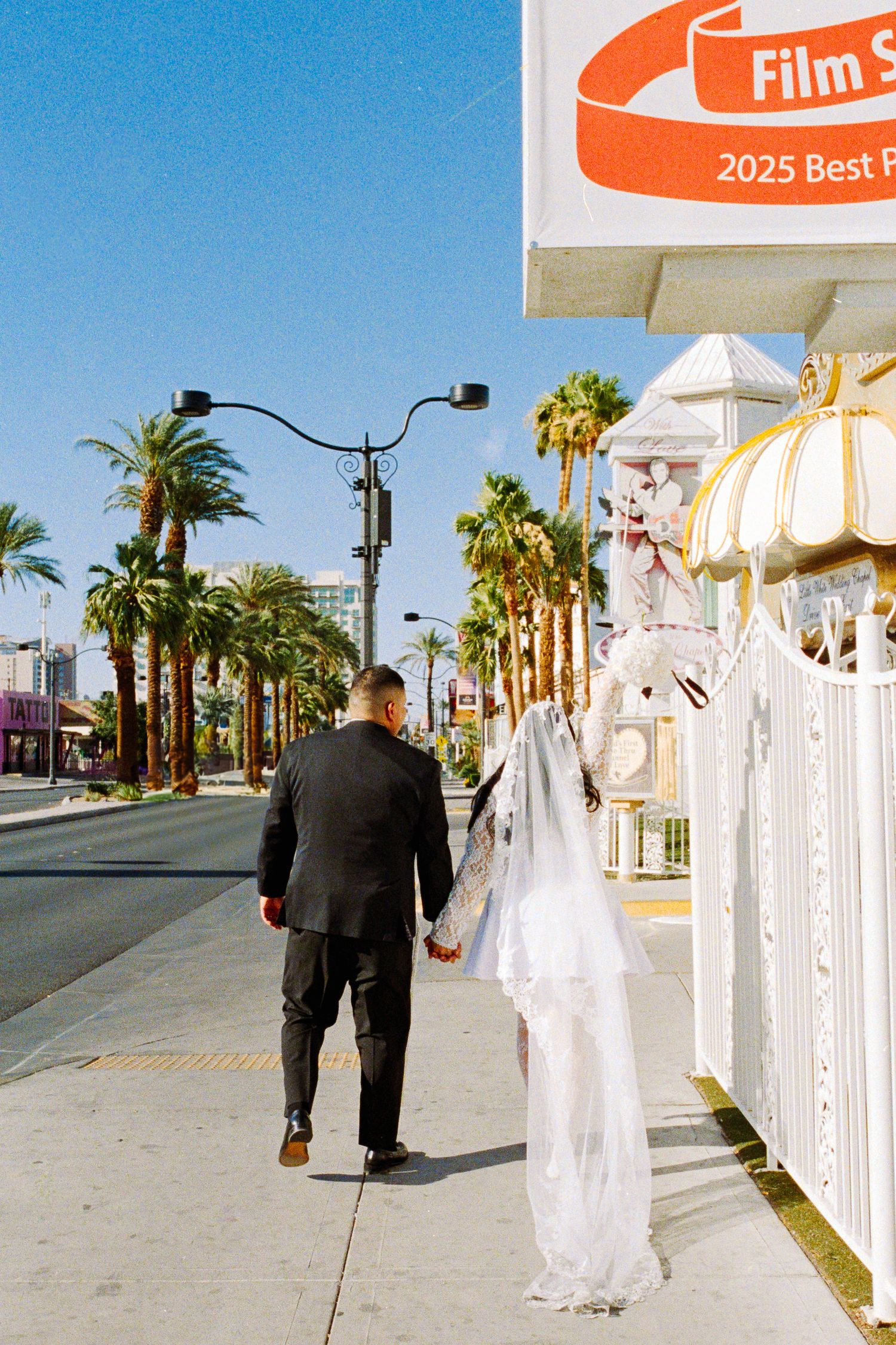 A couple walks hand in hand down a palm-lined Las Vegas street.