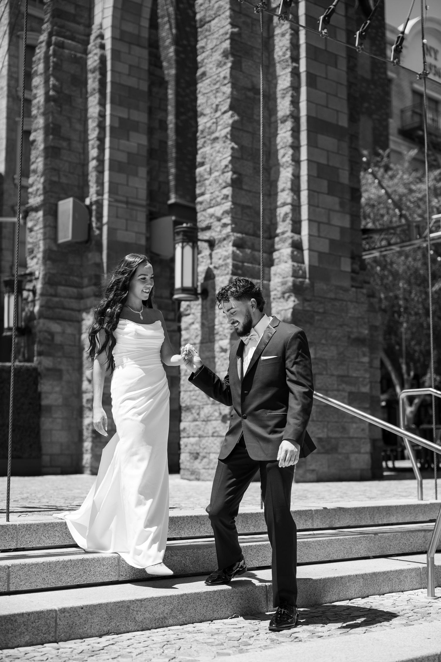 A black and white photo of newlyweds posing playfully on stone steps.