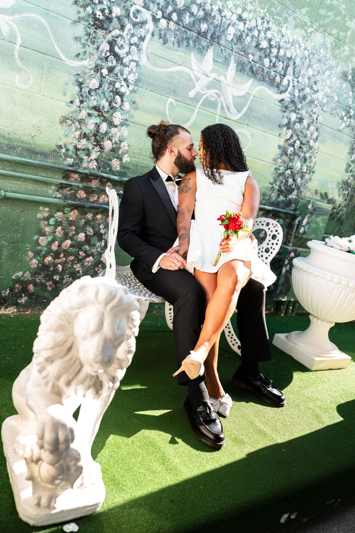A romantic wedding photoshoot in a garden setting with floral arch and white decorative elements.