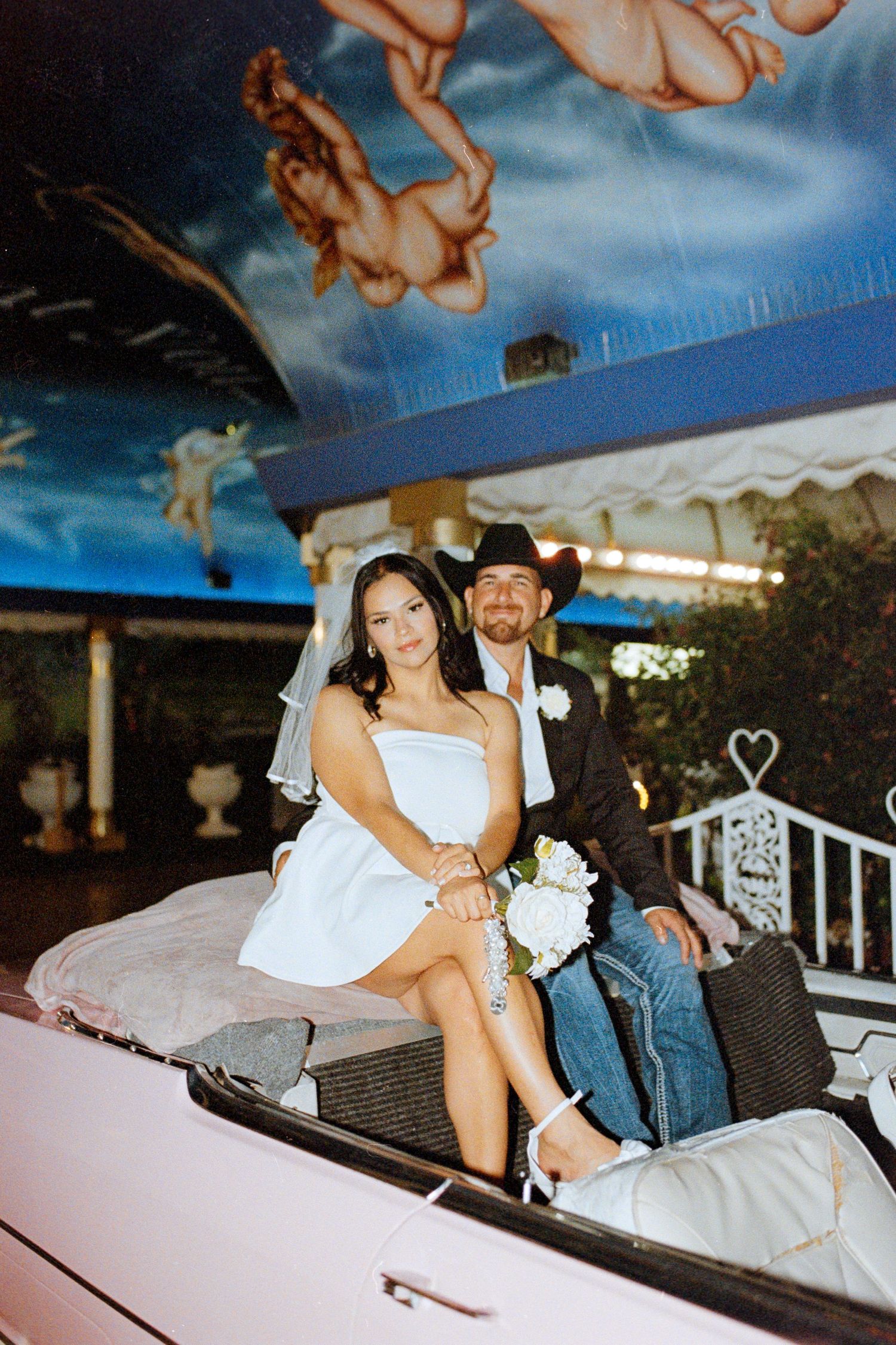 Newlyweds pose together in the back of a vintage car during their wedding celebration.