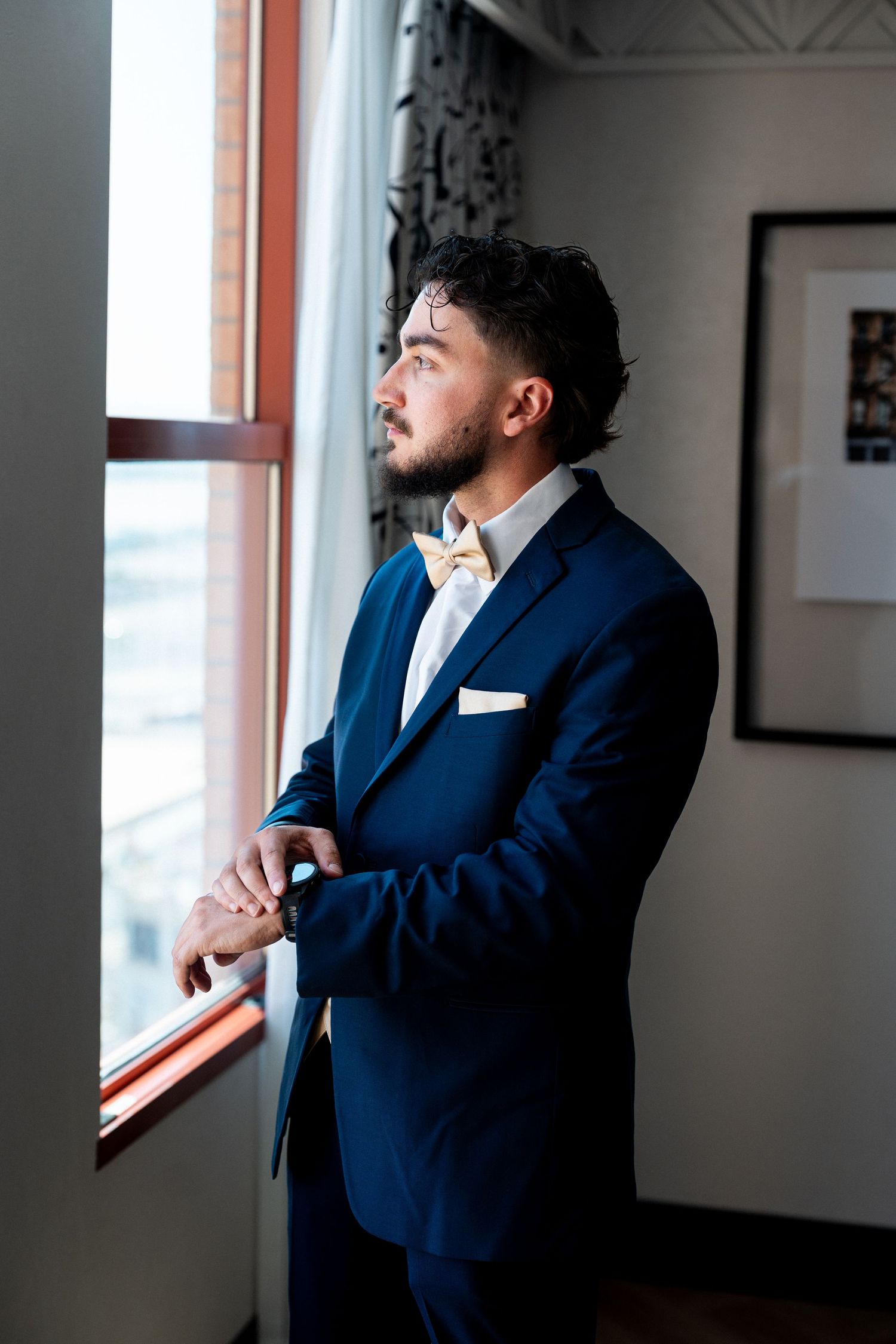 Person in a navy blue suit gazes contemplatively out a bright window.