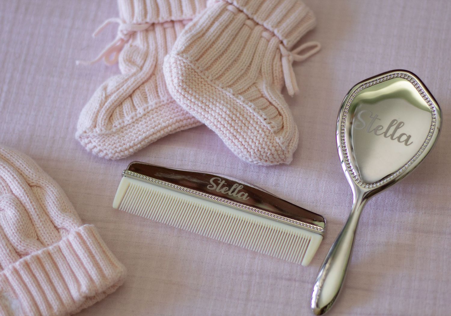 Personalized baby girl gifts including engraved Stella comb, silver mirror, and pink knit mittens.