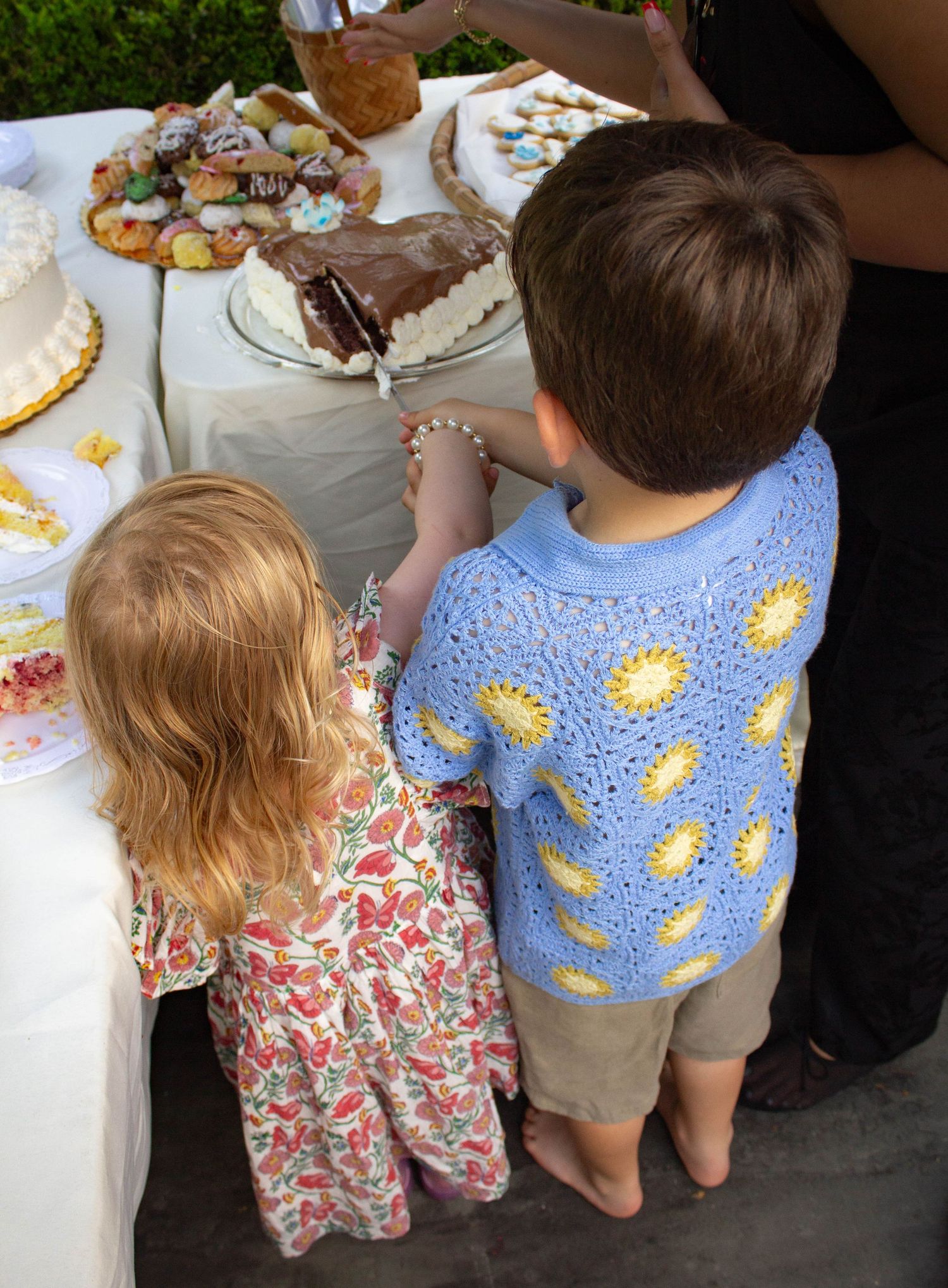 Two young children reaching for cake at an outdoor wedding dessert table.