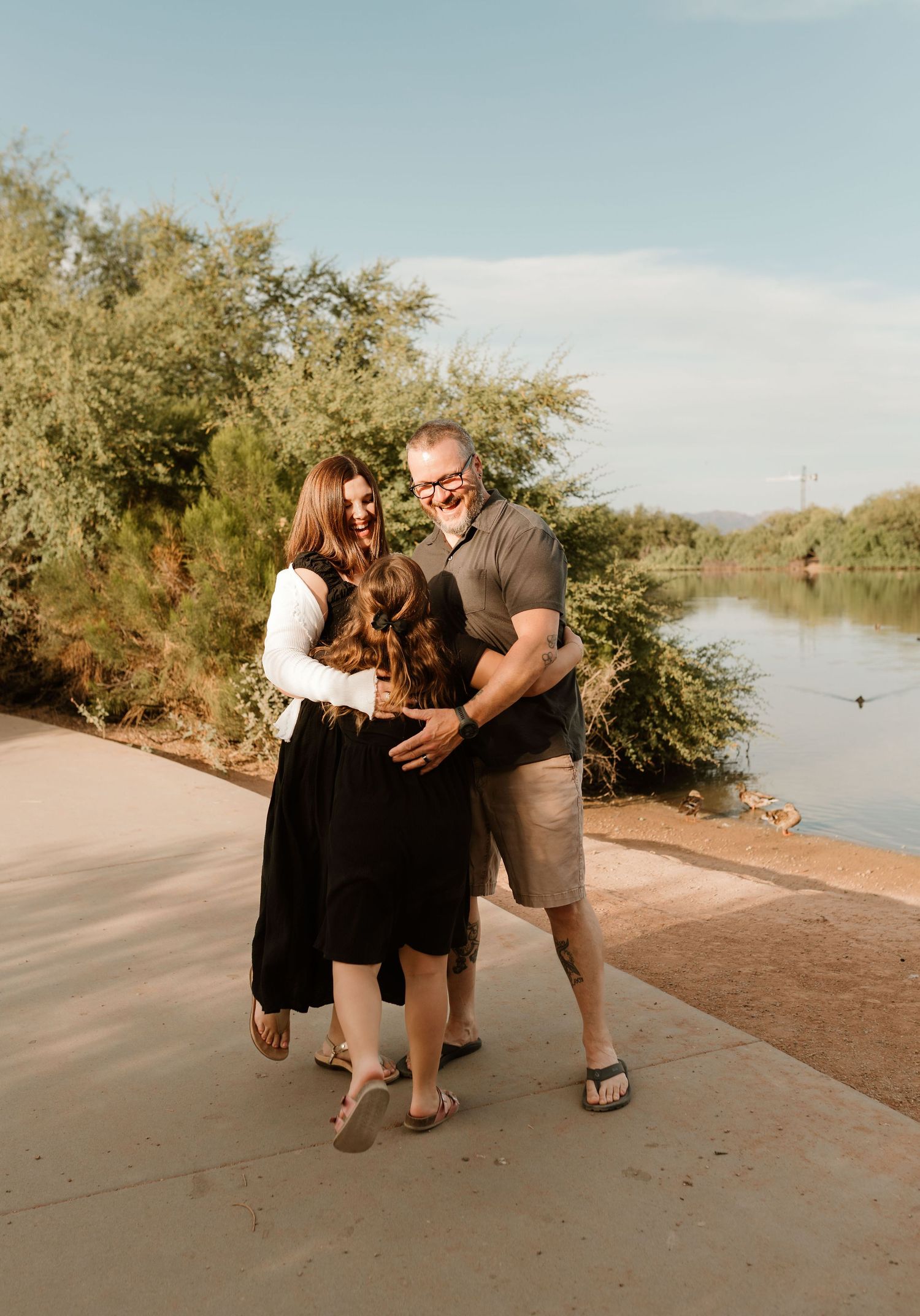 Couple walking along waterfront path with desert vegetation during sunset.