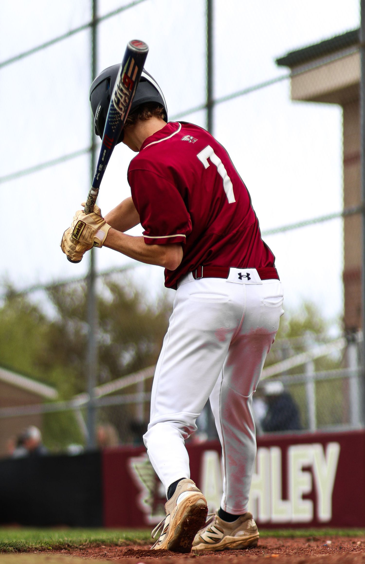 Baseball player wearing number 7 in maroon uniform swings bat during game at Ashley field.