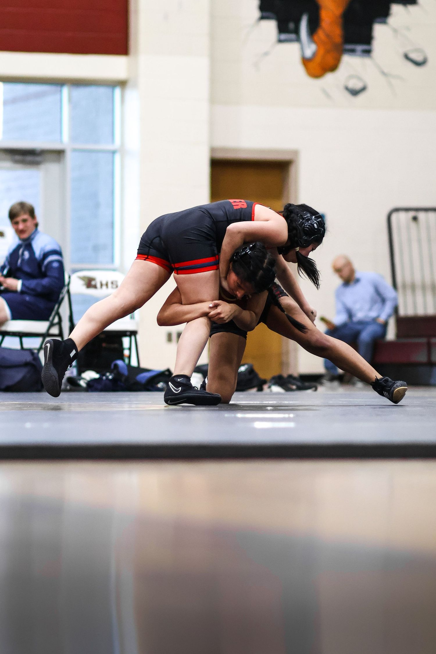 Two wrestlers grappling on a mat during a competitive wrestling match in a gymnasium.