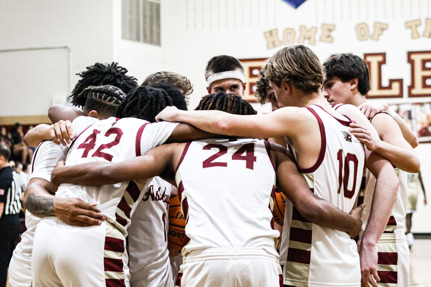 Basketball players huddle together with arms linked in unity before a game at a sports venue.