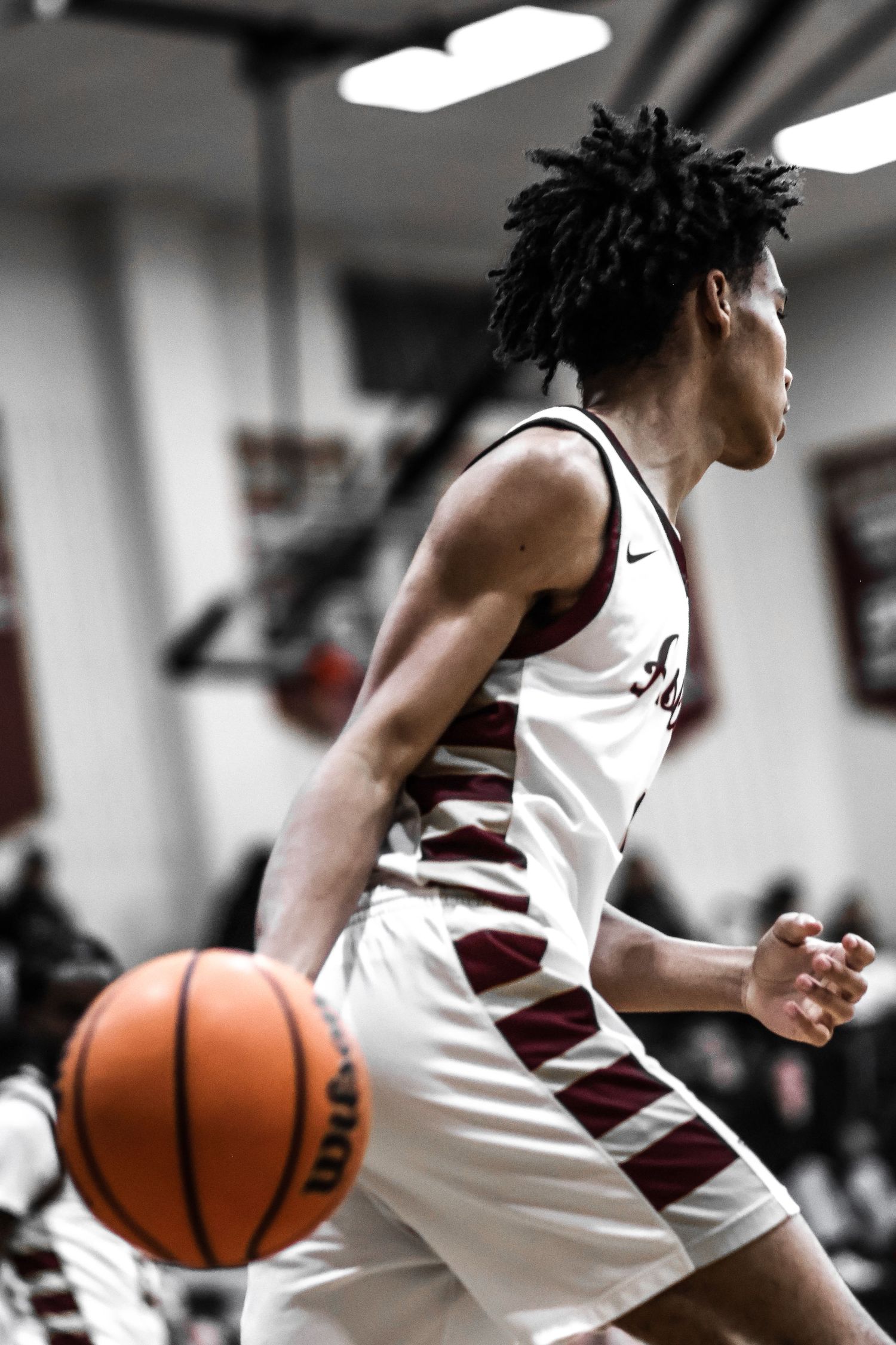 Basketball player in white uniform dribbles down court during intense game action.