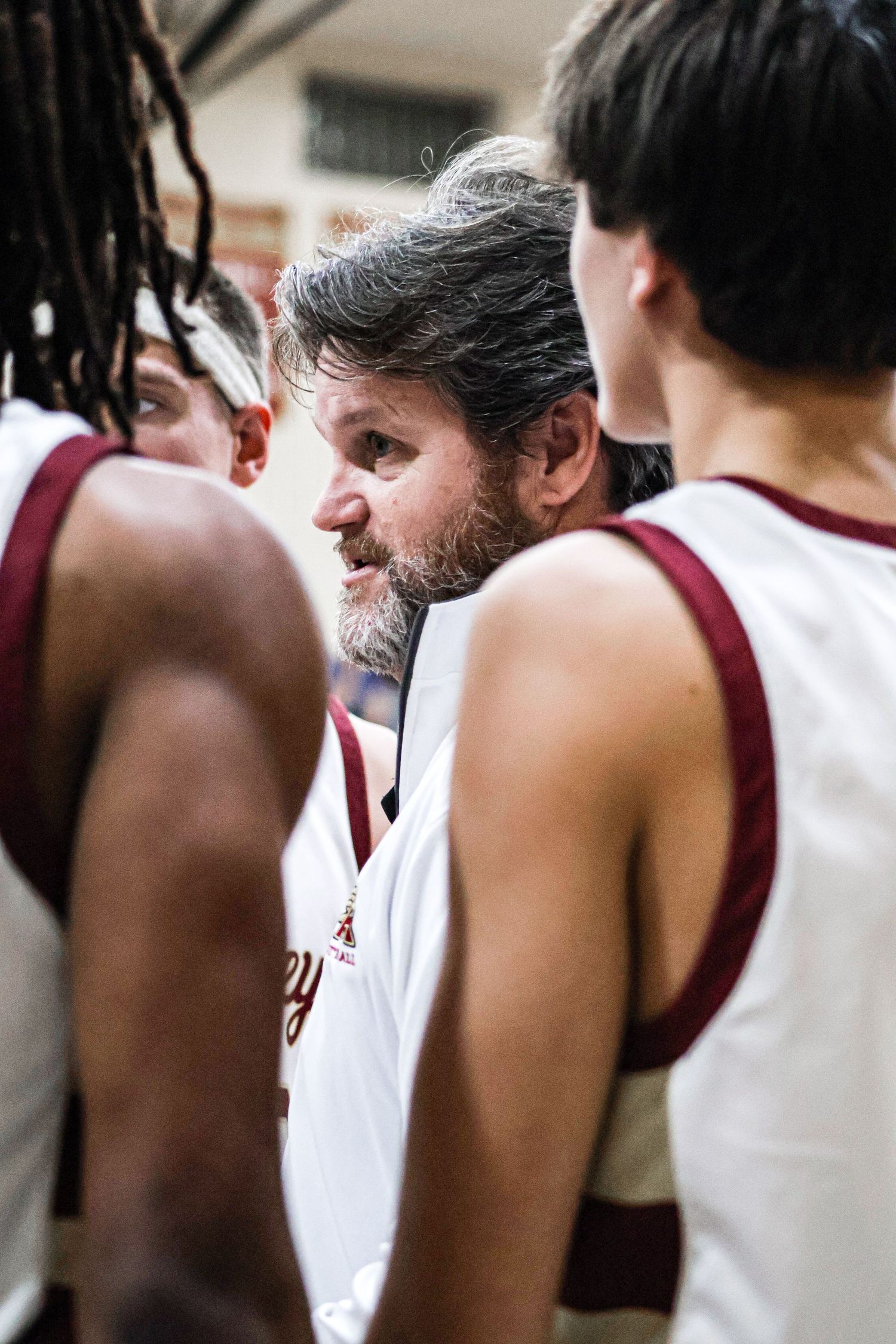Basketball players in maroon and white uniforms huddle together during a game or practice session.