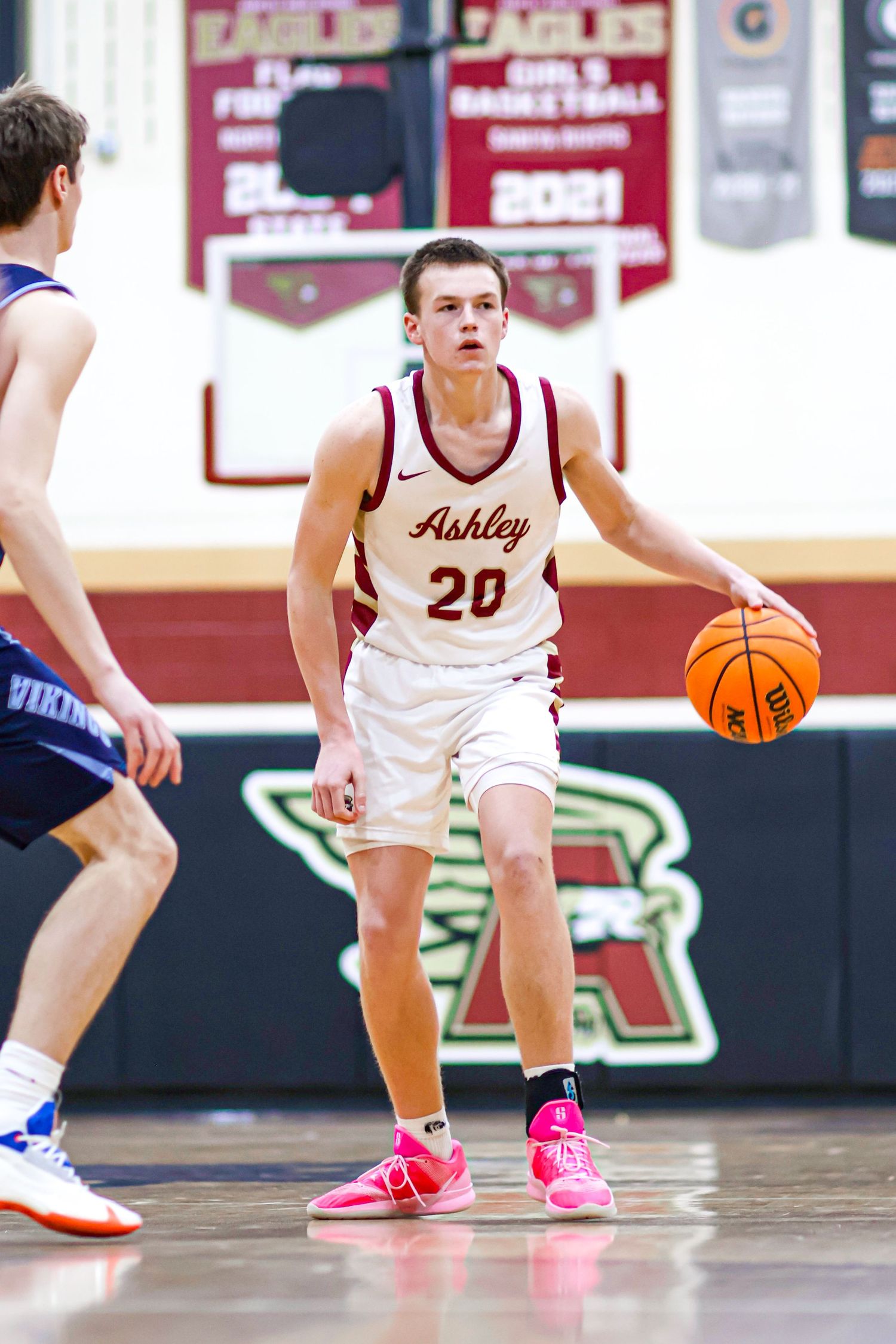 Basketball players wearing pink shoes dribble on the court during a game.