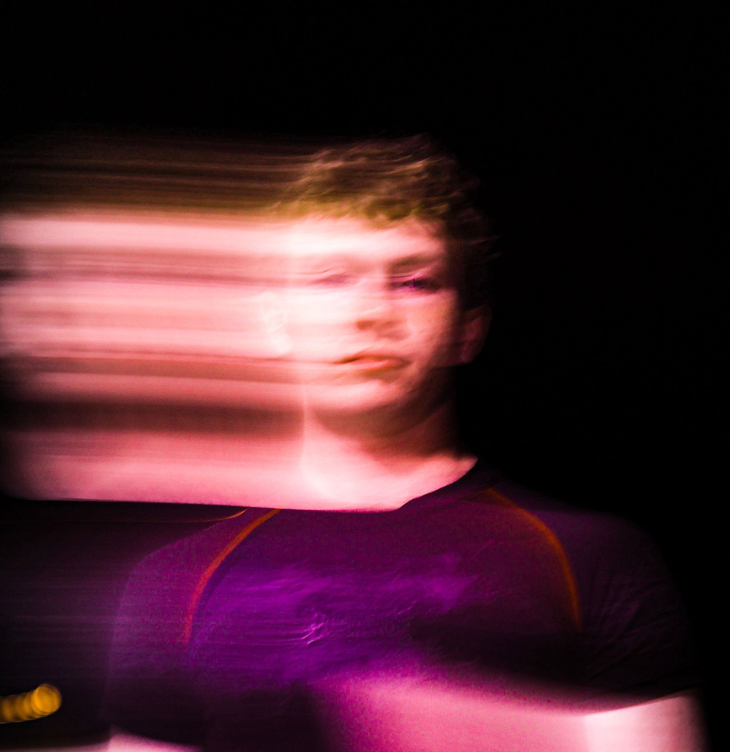 Motion blur portrait of a young person in a purple shirt against a dark background, creating a dreamy effect.