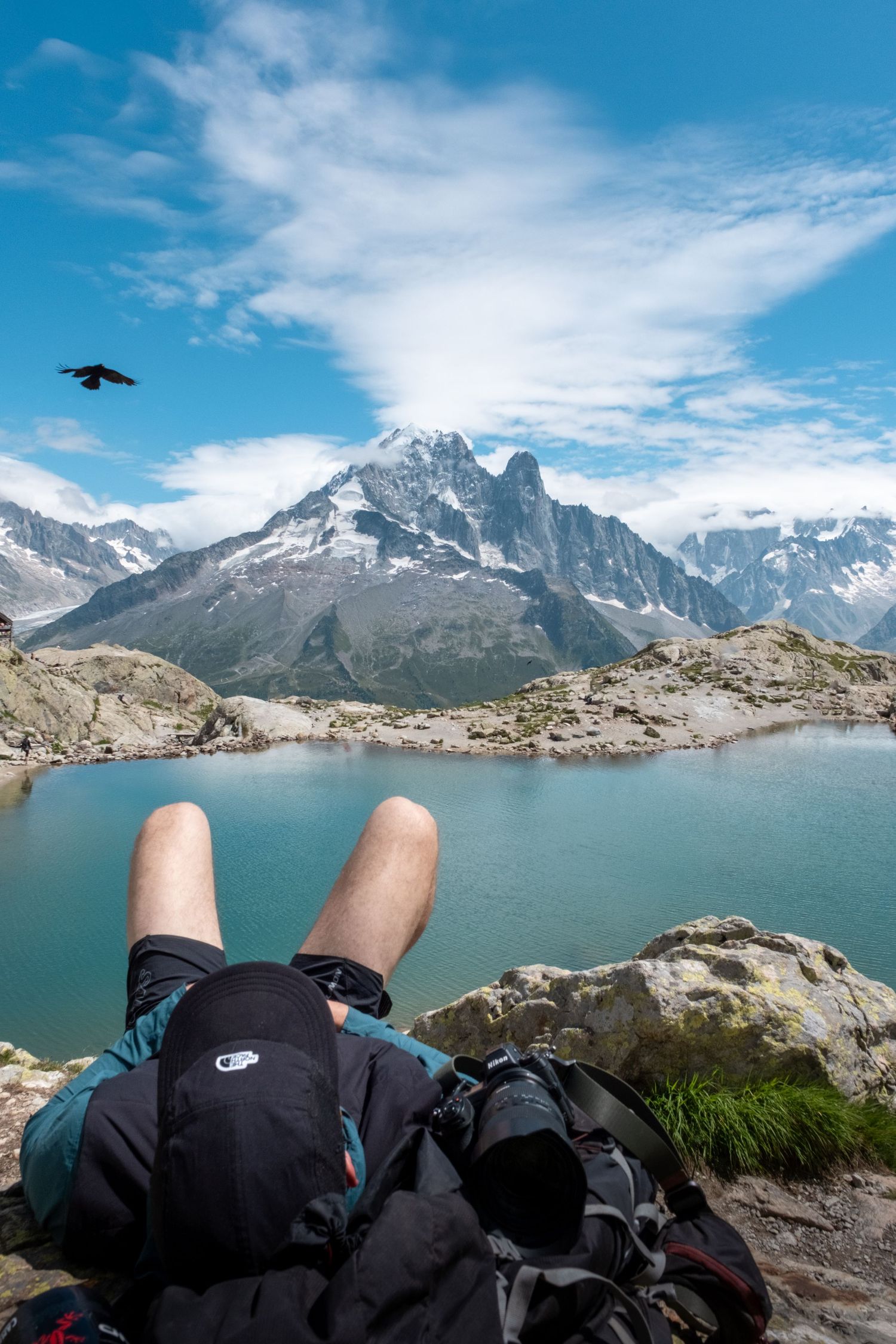 Hiker resting on rocky alpine terrain with stunning mountain lake and snow-capped peaks backdrop.